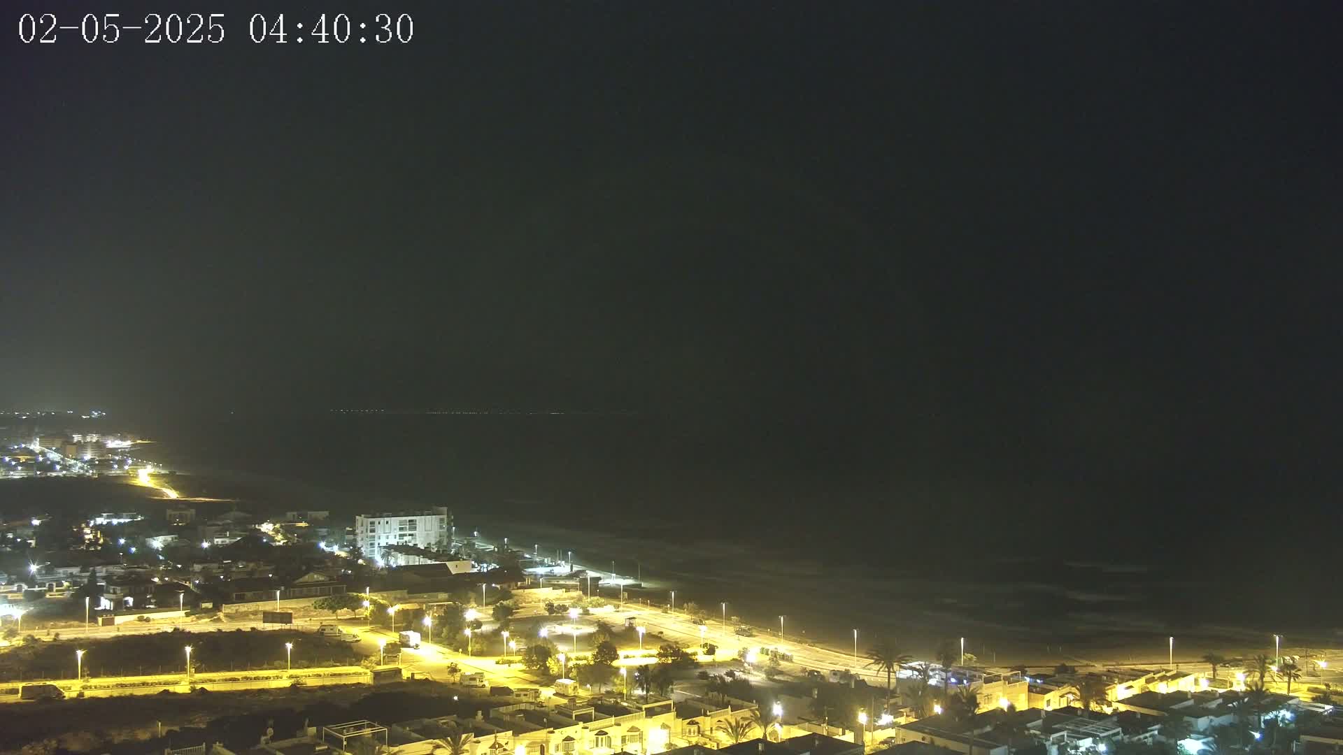 A nighttime view of a coastal town with its lights illuminating the beach and ocean under a dark sky.