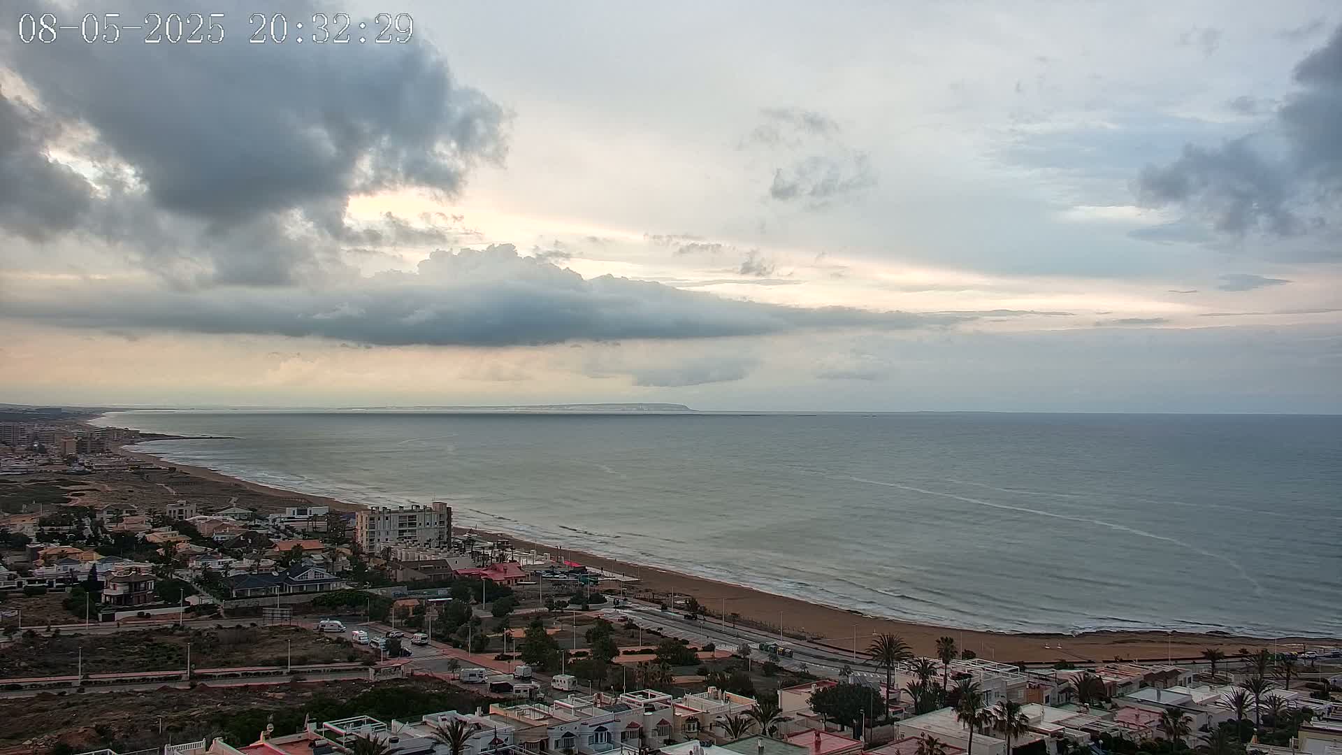 A coastal town overlooks a wide, calm ocean under a cloudy, overcast sky.