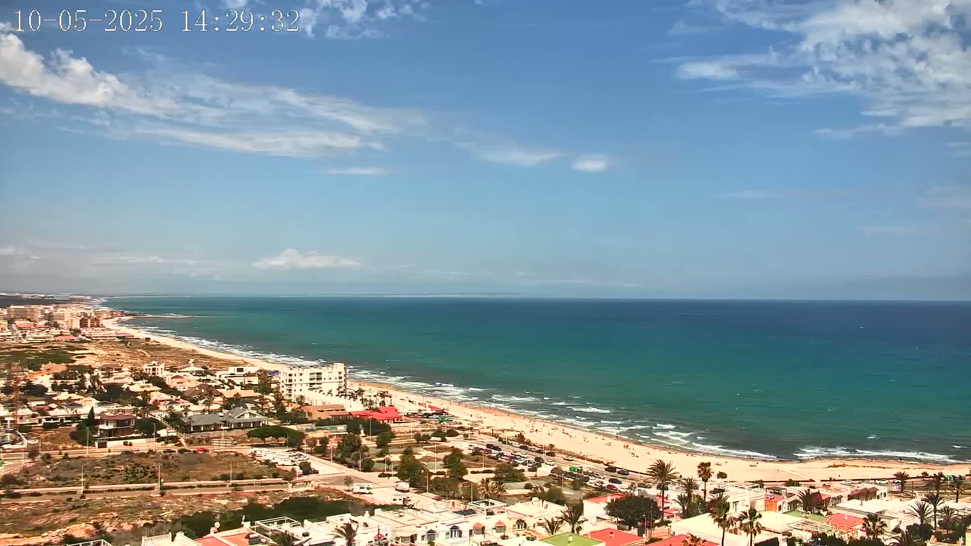 A coastal town on a sunny day with a partly cloudy sky and a long sandy beach with turquoise water.