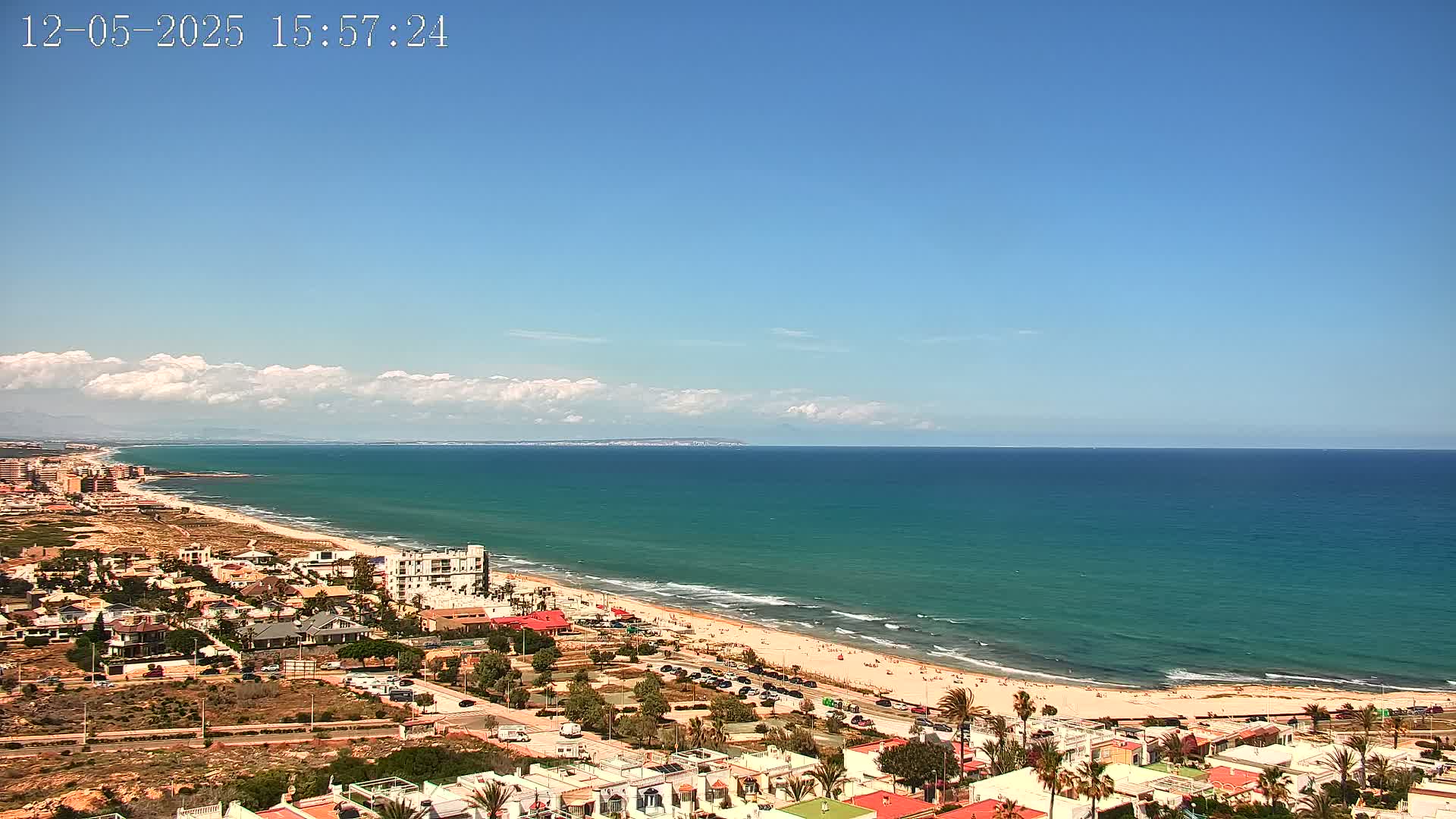 A coastal town overlooks a wide, turquoise ocean under a mostly clear blue sky with a few fluffy clouds.