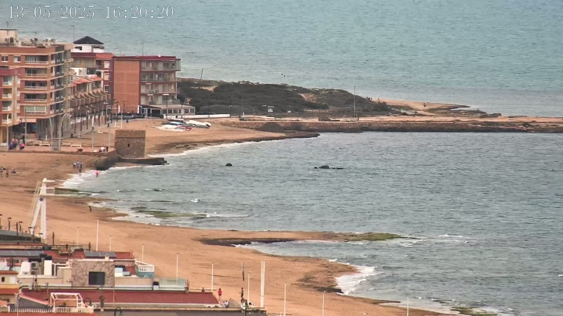 A sandy beach with a calm sea and several buildings is visible from an elevated viewpoint.