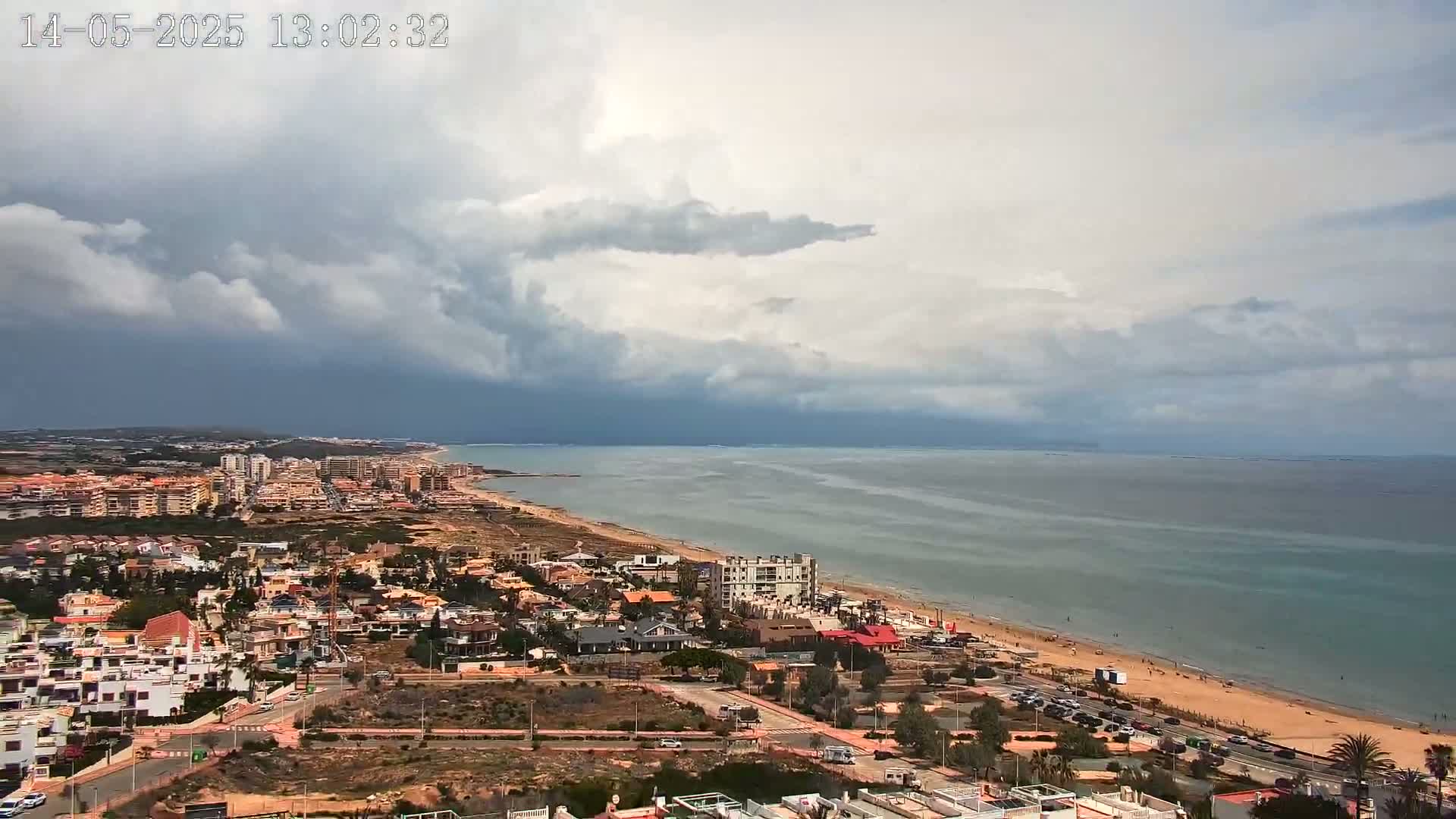 A coastal town with a sandy beach and calm sea is visible under a partly cloudy sky.