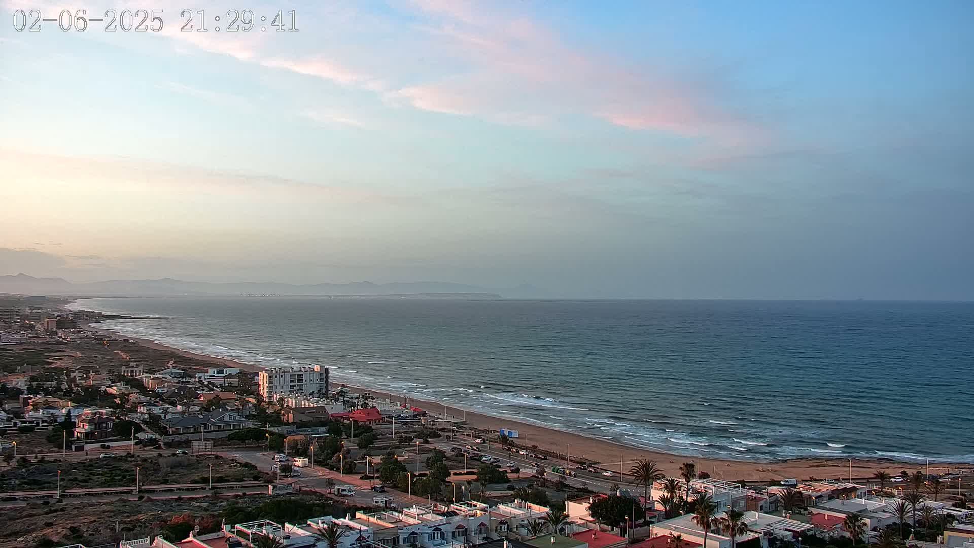 A coastal town overlooks a calm ocean under a pale, pinkish-blue twilight sky.