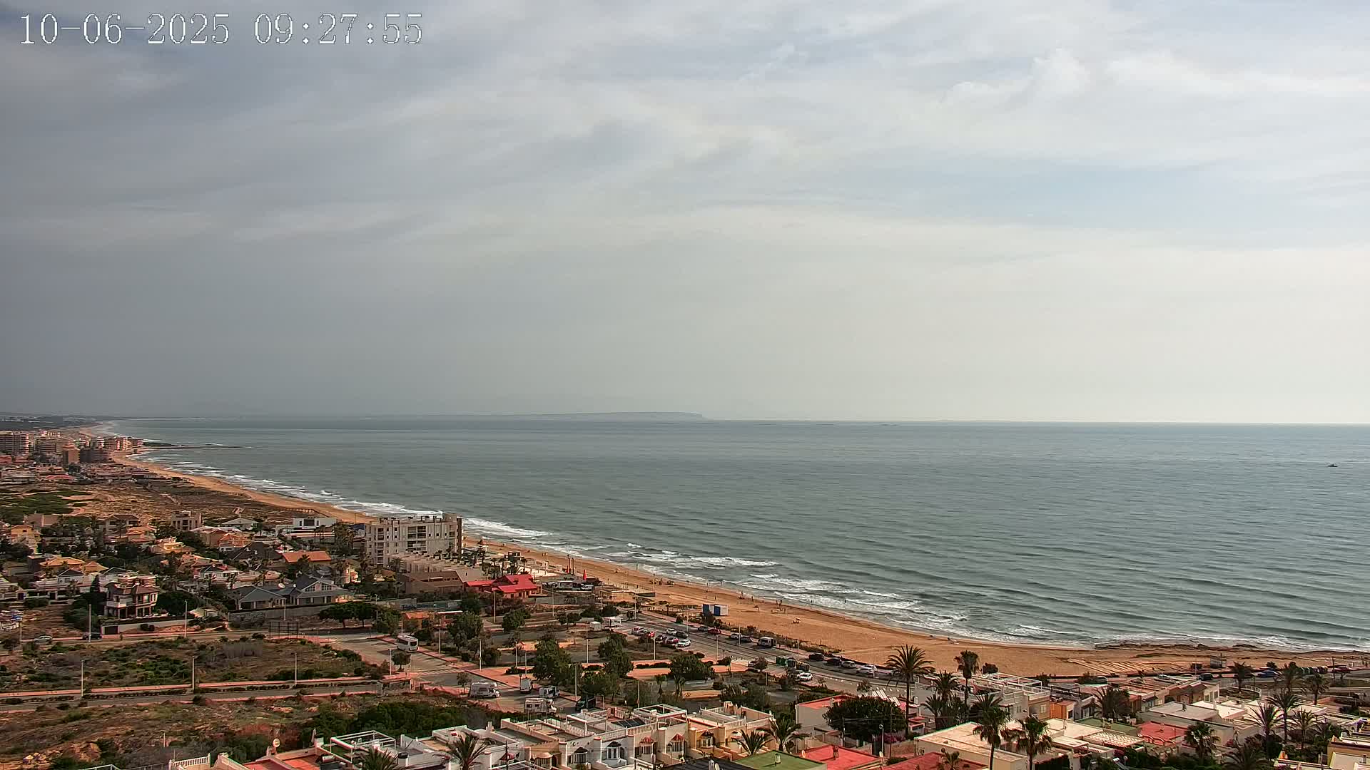An overcast sky overlooks a coastal town with a sandy beach and calm ocean waves.