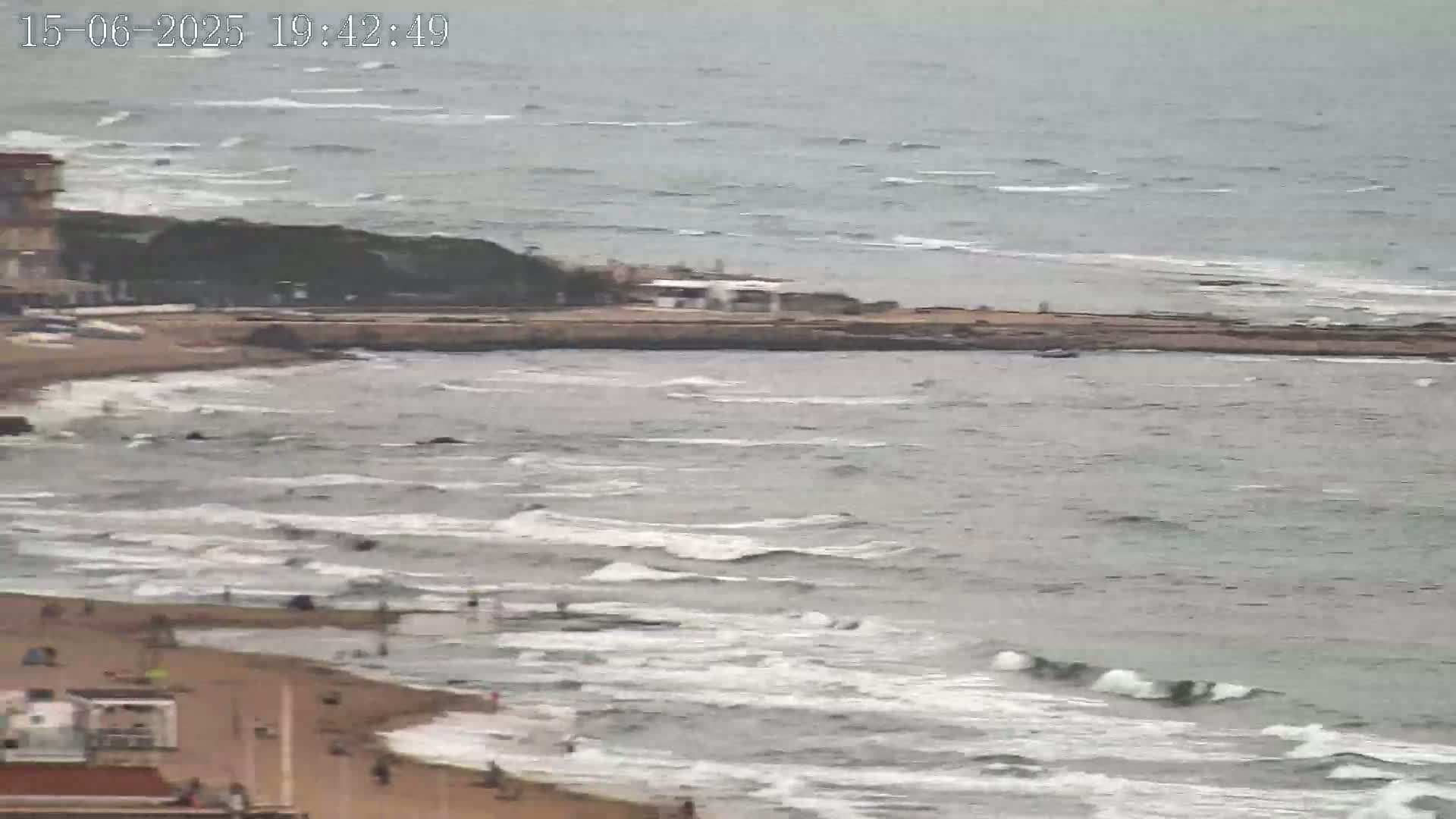 A sandy beach with moderate waves under an overcast sky.