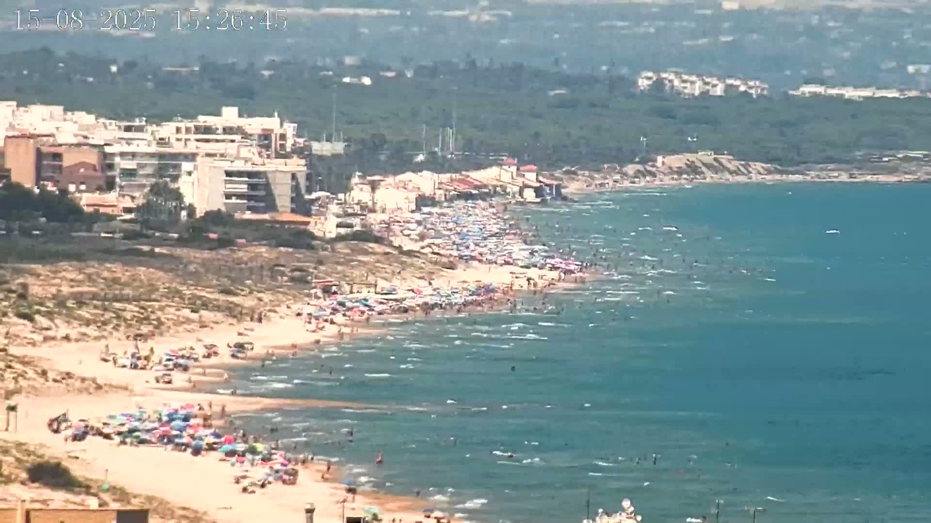 A calm, hazy ocean scene shows several people in the water near a sandy beach.