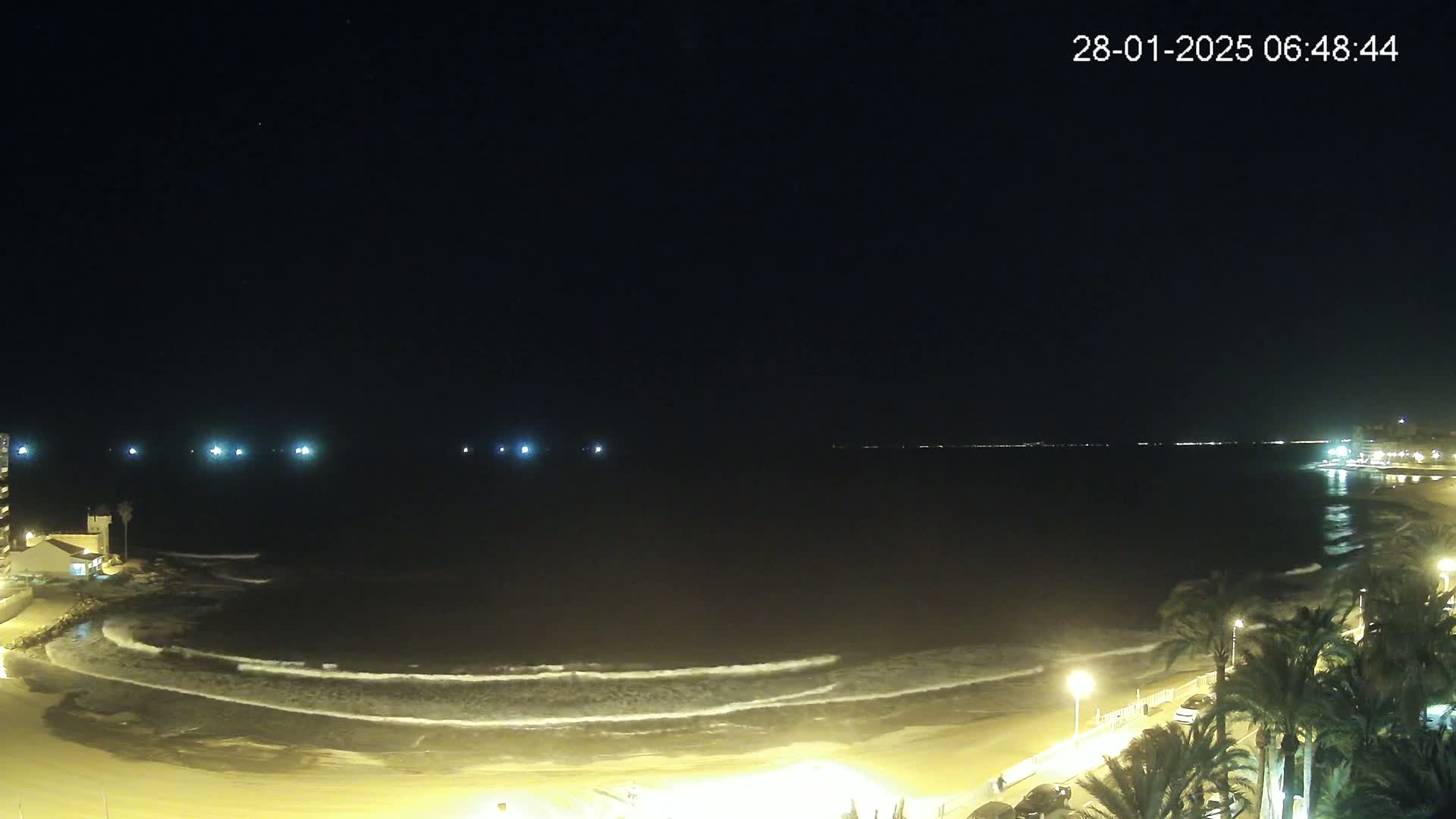 A nighttime beach scene shows gentle waves lapping the shore under a dark sky.