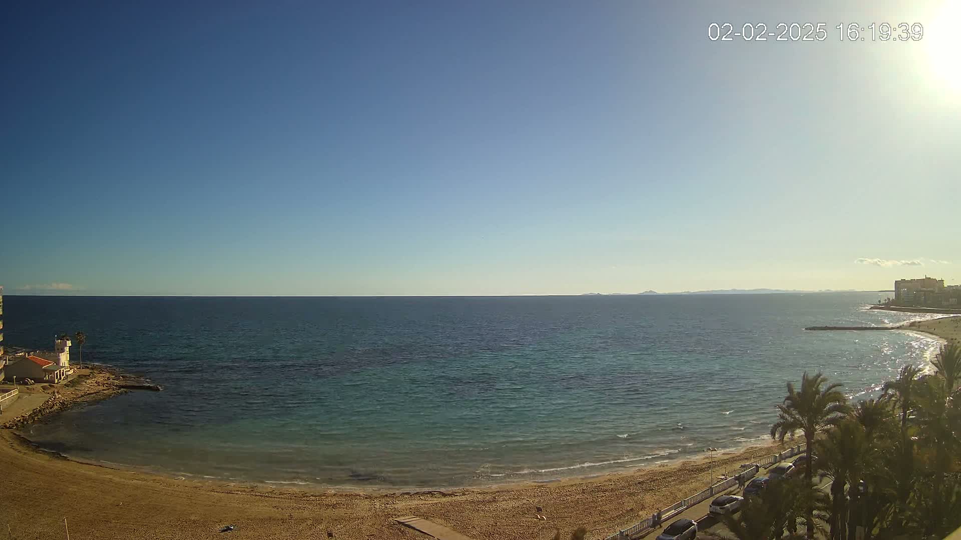 A sandy beach curves around a calm, teal ocean under a clear blue sky.