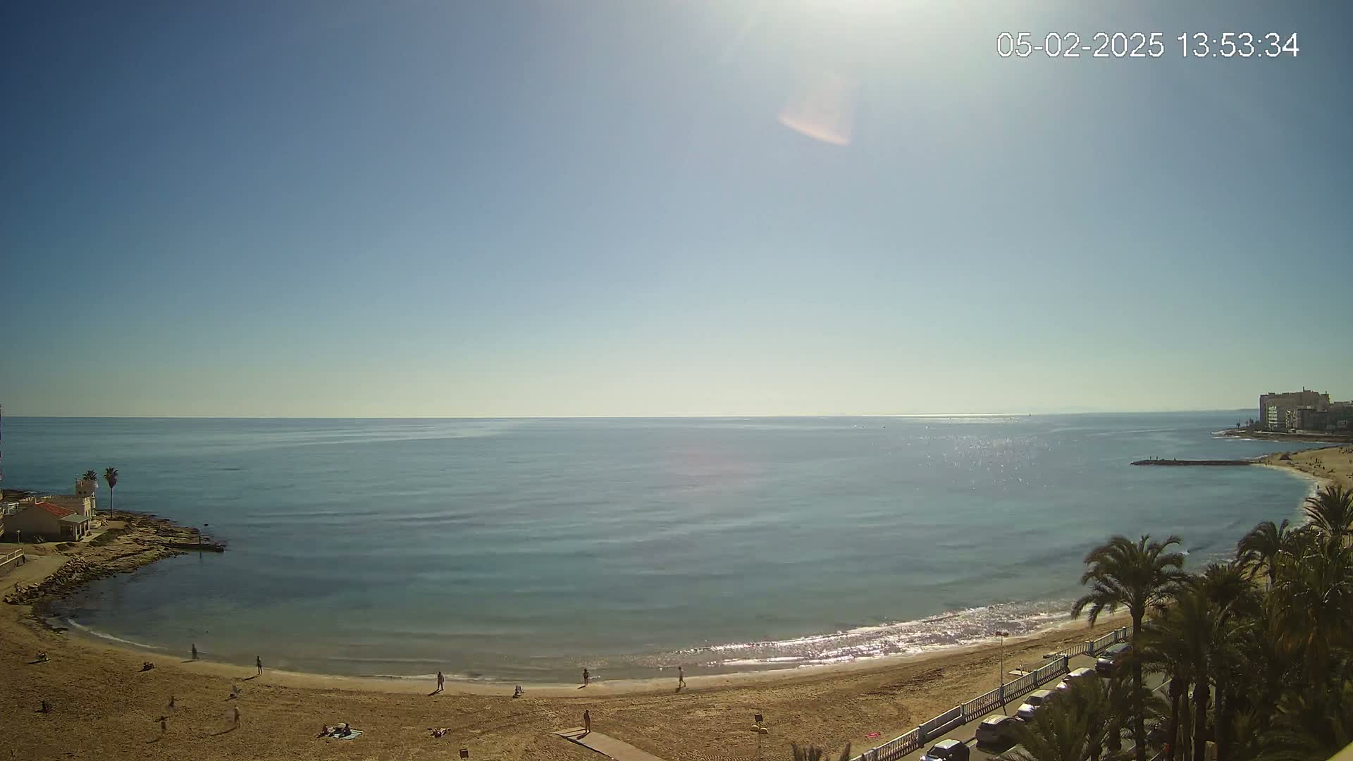 A sandy beach curves around a calm, blue sea under a clear, sunny sky.