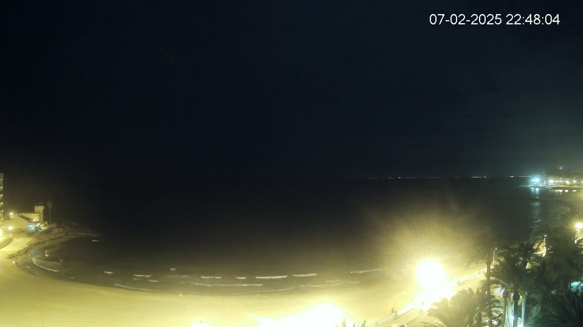 A nighttime view of a beach with gently lapping waves under a dark, clear sky.