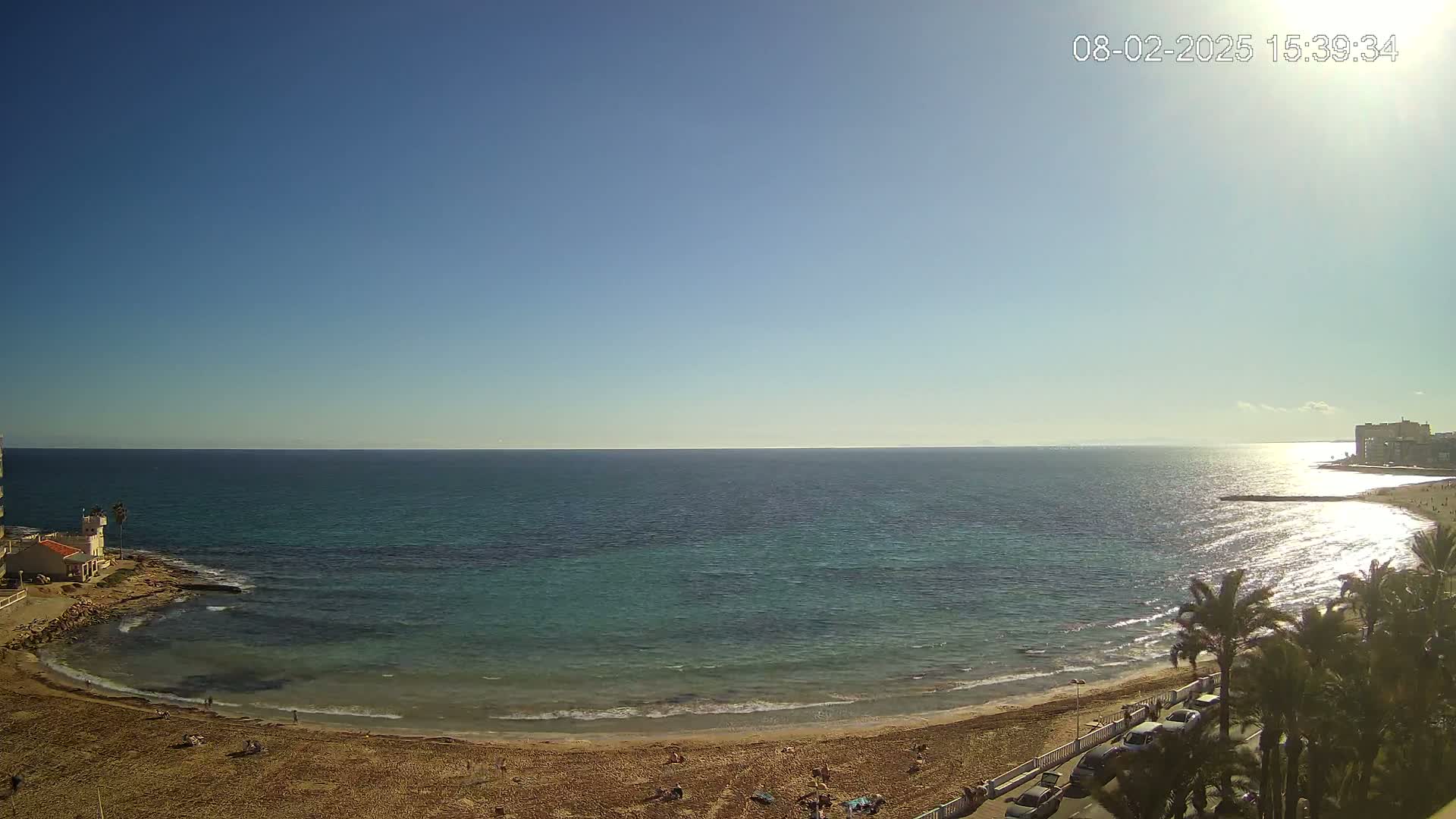 A sandy beach curves along a calm, turquoise sea under a clear, sunny sky.
