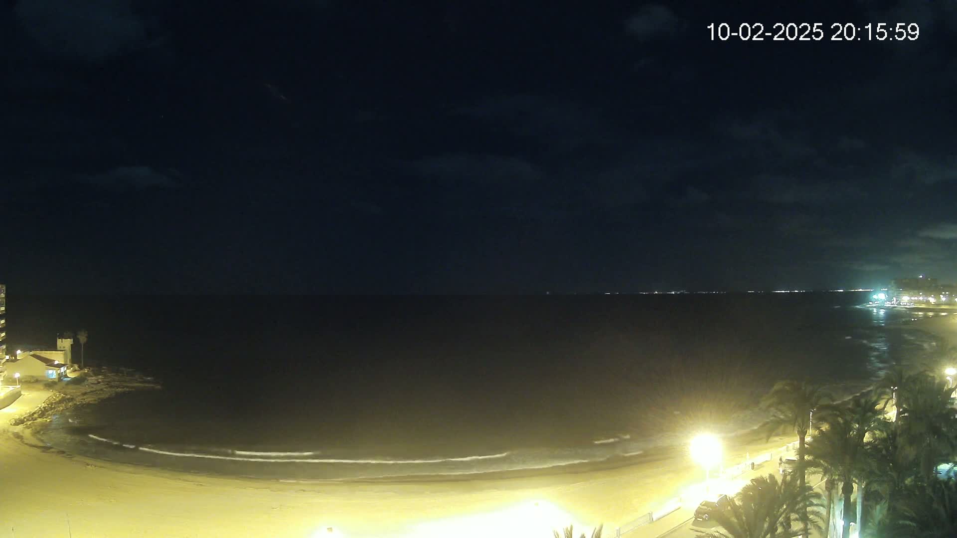A nighttime view of a beach with gentle waves lapping the shore under a partly cloudy sky.