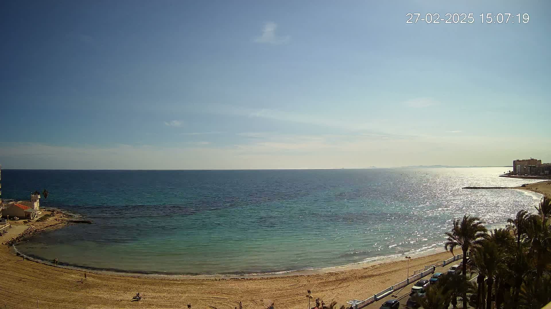 A sandy beach curves around a calm, turquoise sea under a clear blue sky.