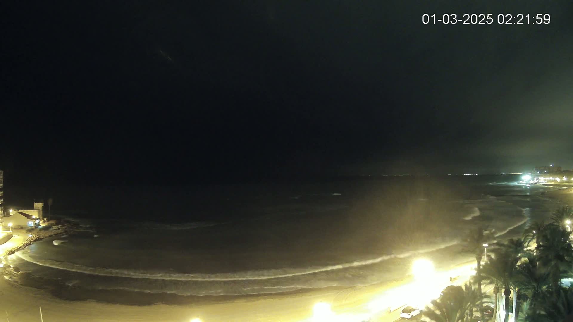 A nighttime view of a beach with gentle waves rolling onto the shore under a dark sky.