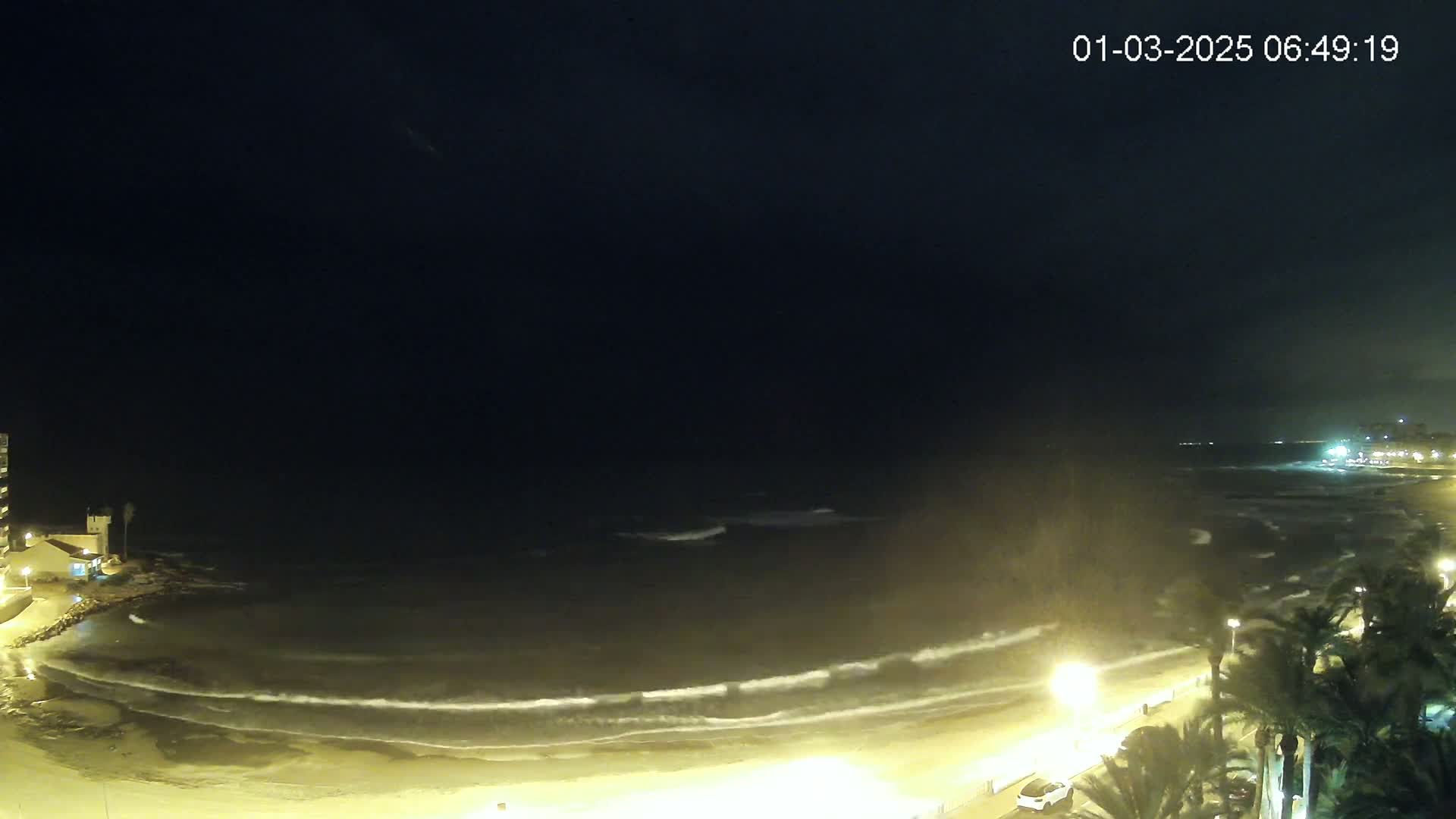 A nighttime view of a beach with gently rolling waves under a dark sky.