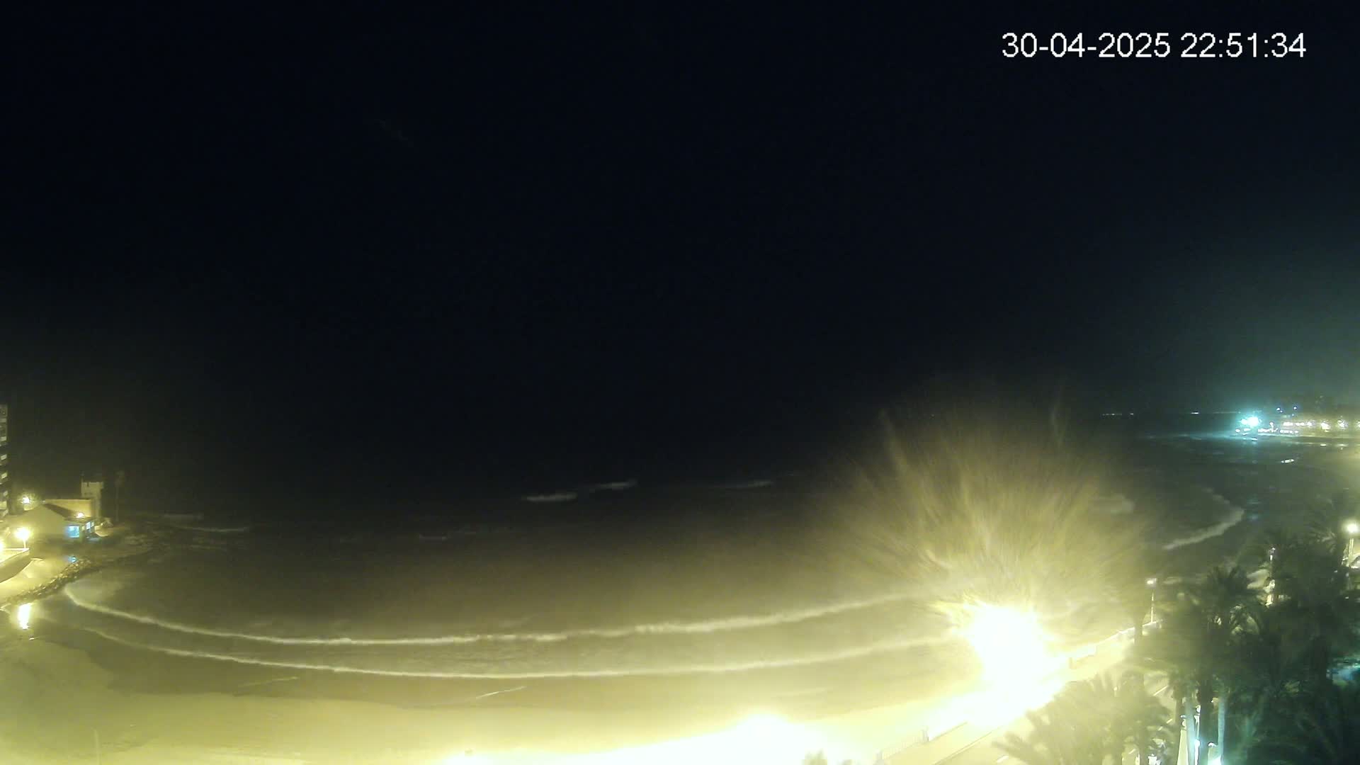 A nighttime view of a beach with gently lapping waves under a dark sky.