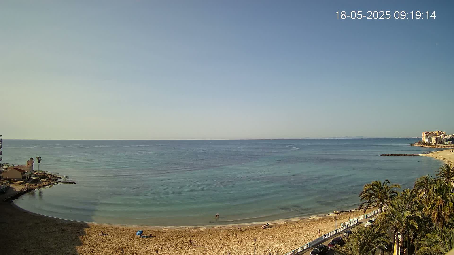 A sandy beach curves around a calm, turquoise ocean under a clear, light blue sky.