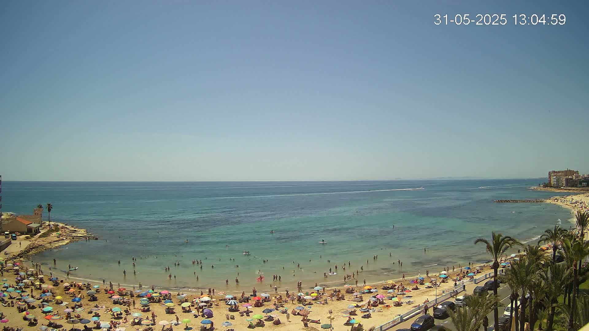 A crowded beach with colorful umbrellas under a clear blue sky and calm, turquoise water.