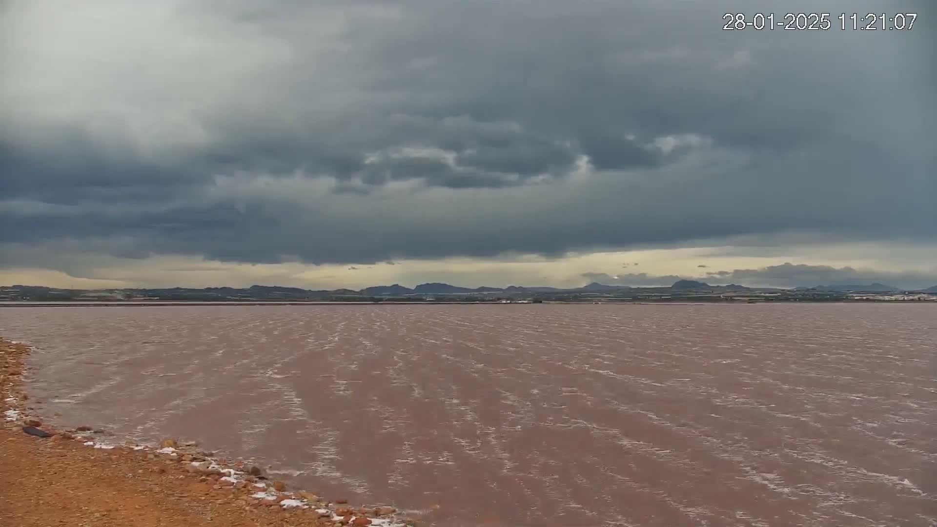 A pinkish-brown body of water stretches to a distant, hilly landscape under a cloudy, overcast sky.