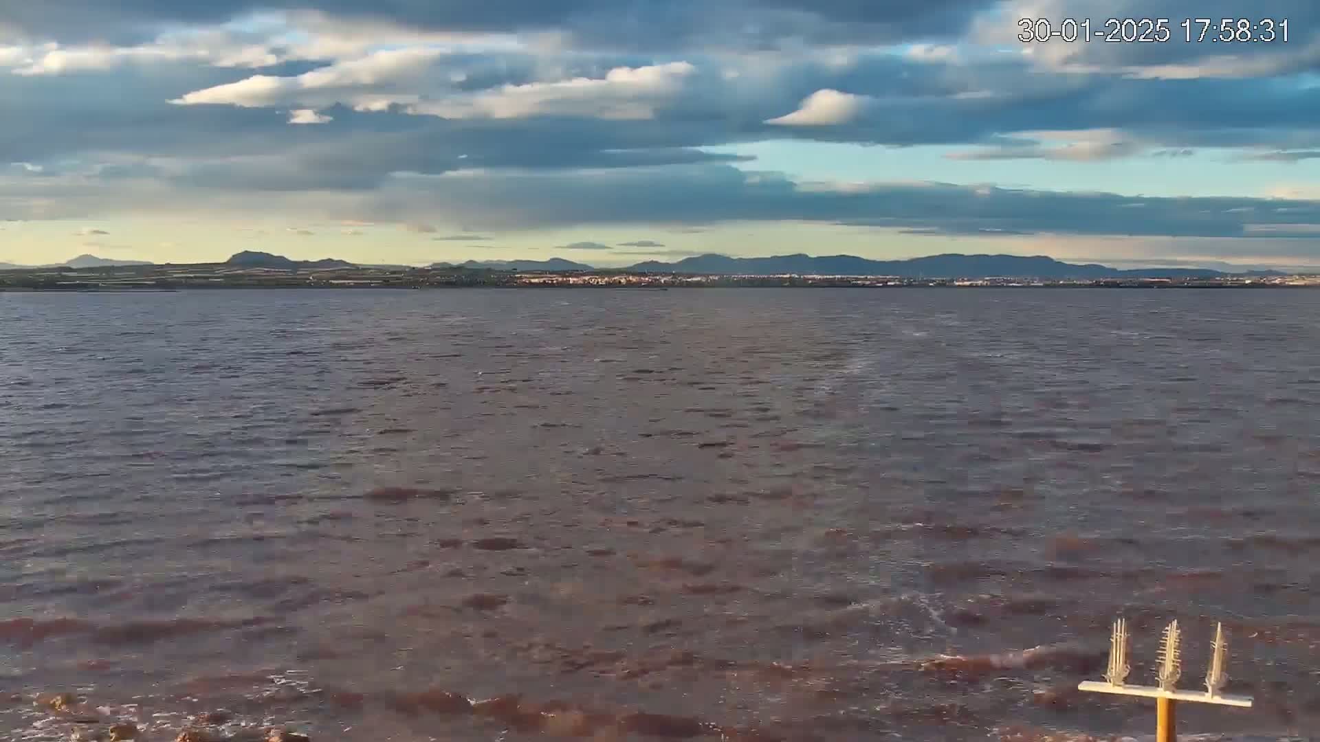 A body of somewhat choppy water with a distant mountain range under a partly cloudy sky.