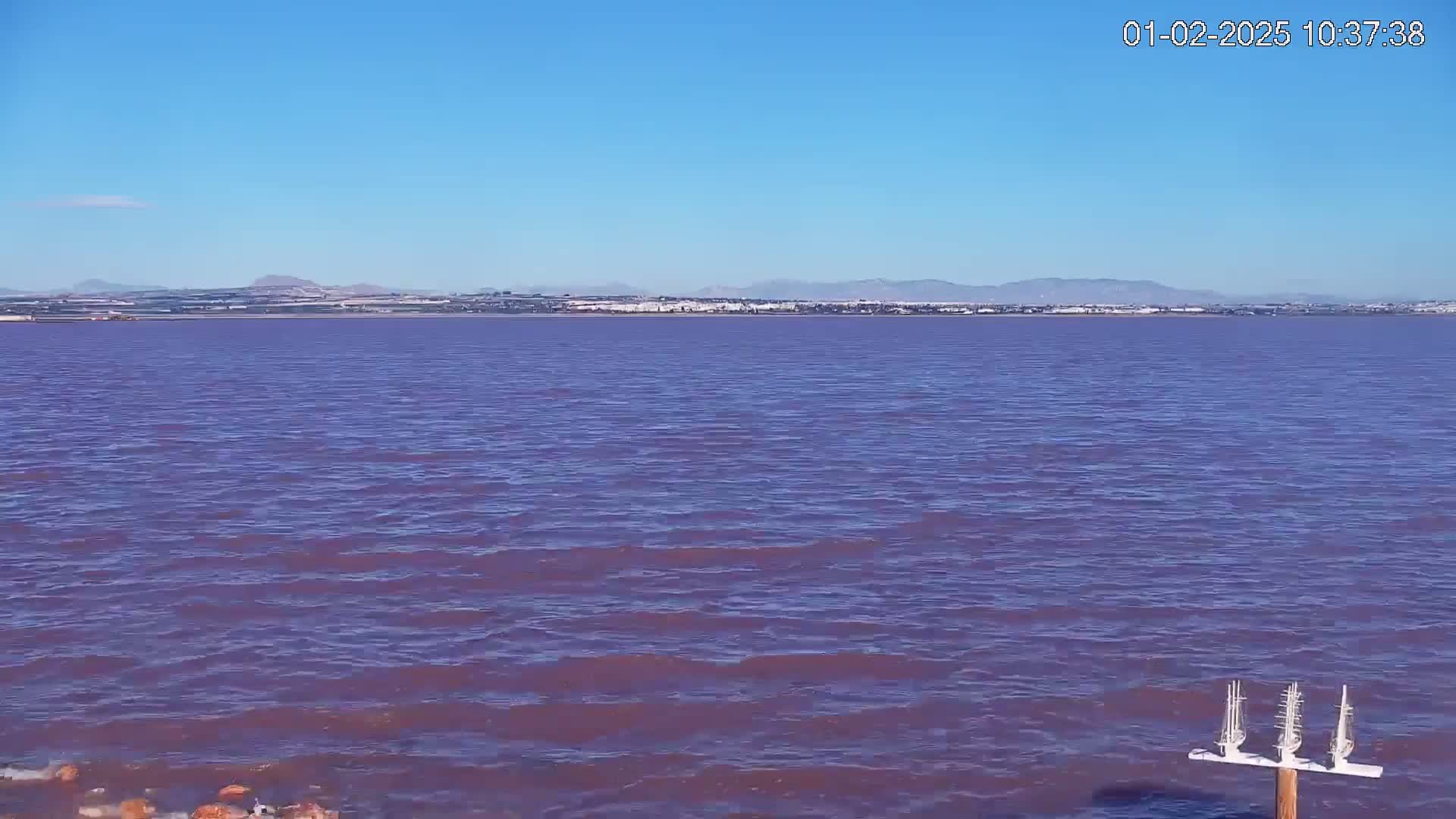 A purplish body of water stretches to a distant shoreline under a clear blue sky.