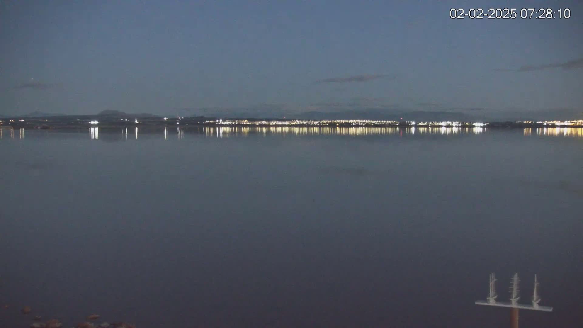 A calm body of water reflects the lights of a distant city at twilight.