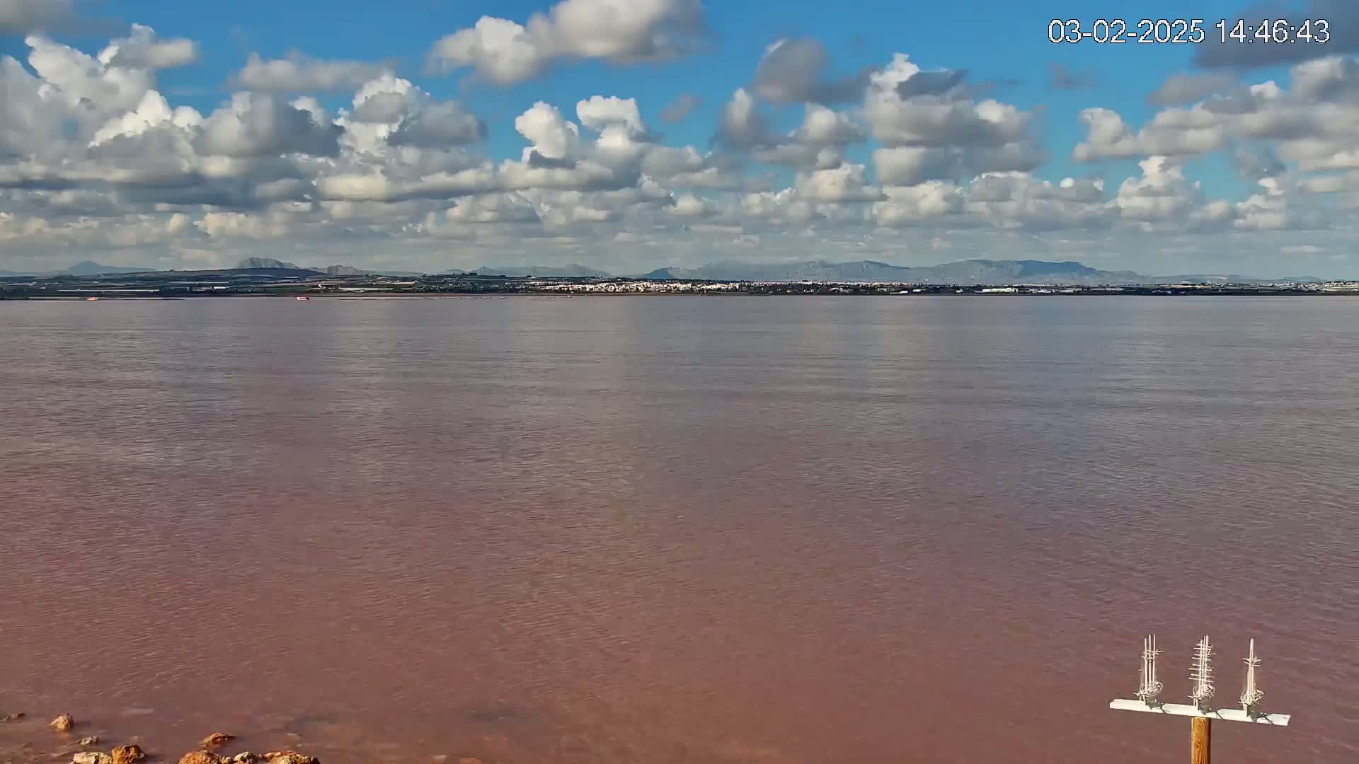 A pinkish body of water stretches out to a distant shoreline under a partly cloudy sky.