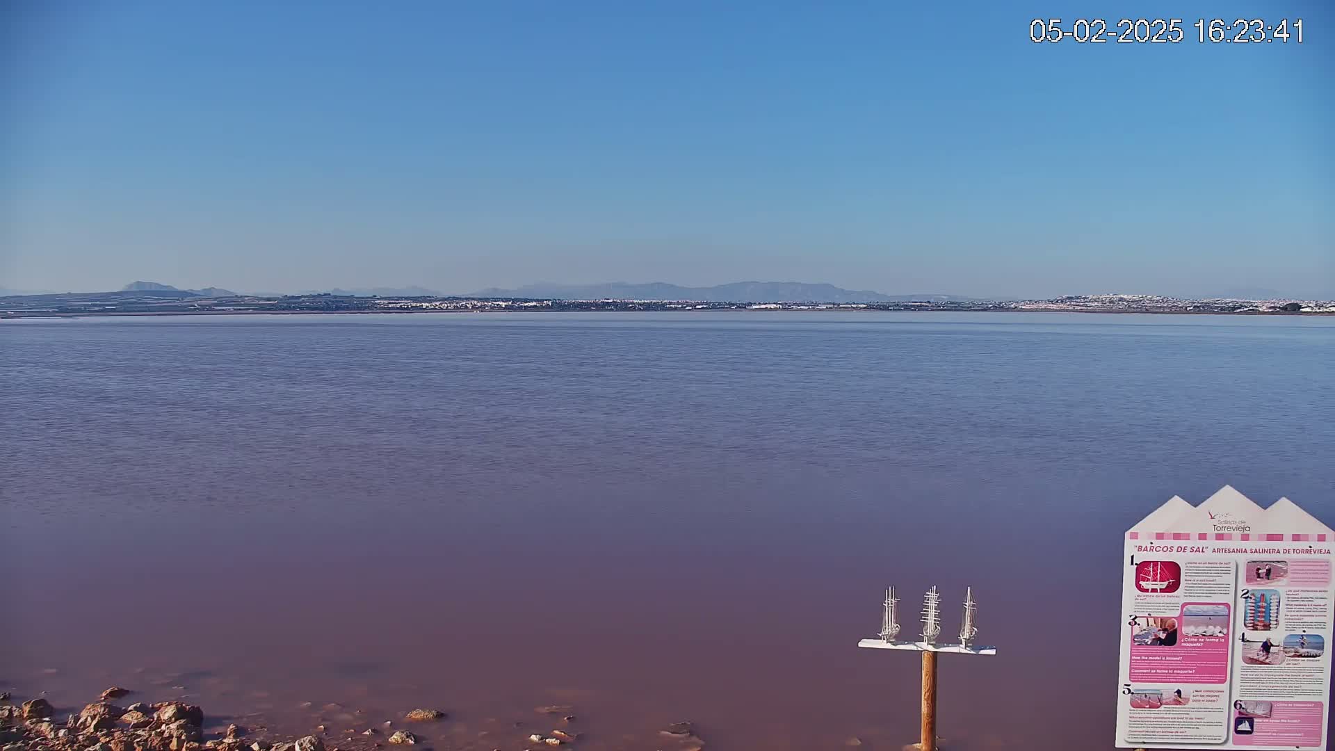 A calm, pinkish body of water stretches to a distant shoreline under a clear blue sky.