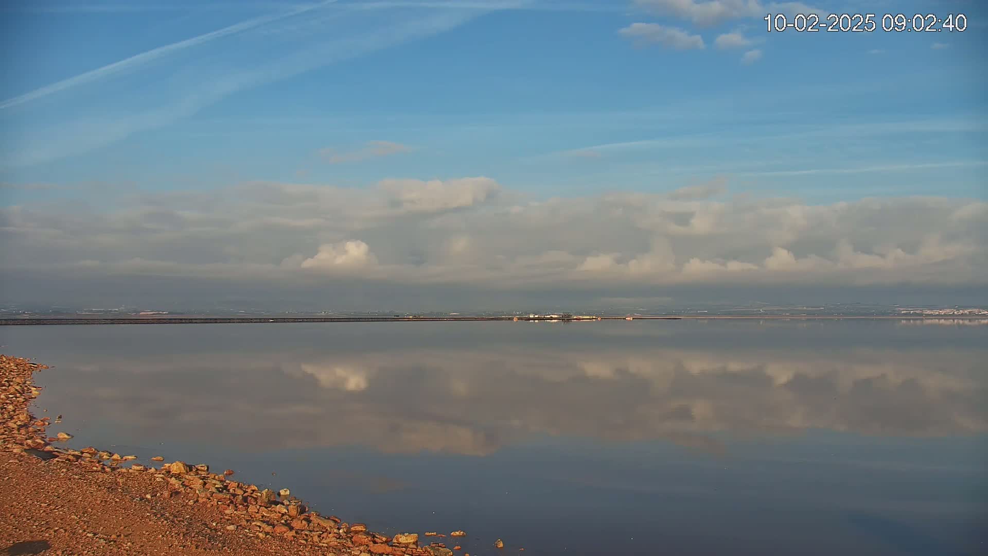 A calm body of water reflects a partly cloudy sky under clear blue skies.
