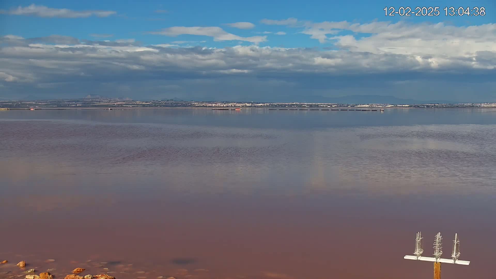 A pinkish-red lake stretches to a distant shoreline under a partly cloudy sky.