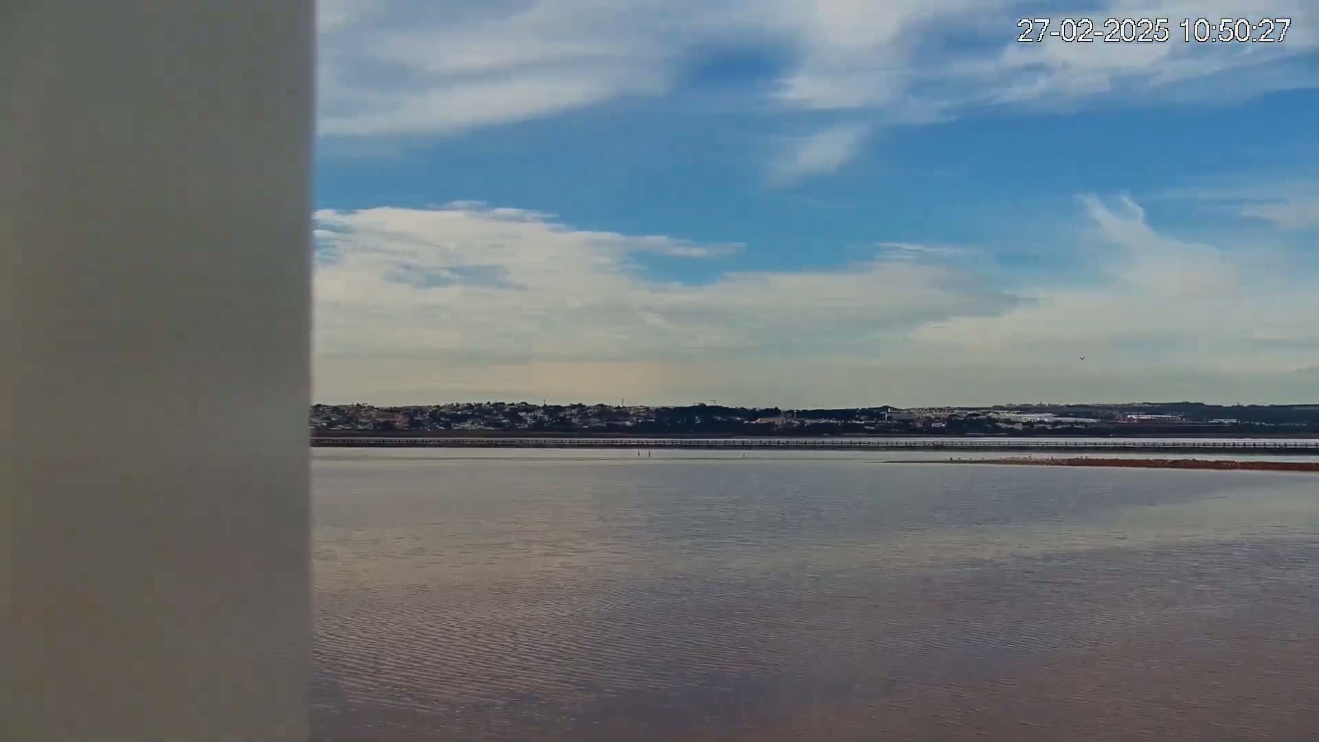 A calm body of water stretches to a distant shoreline under a partly cloudy sky.