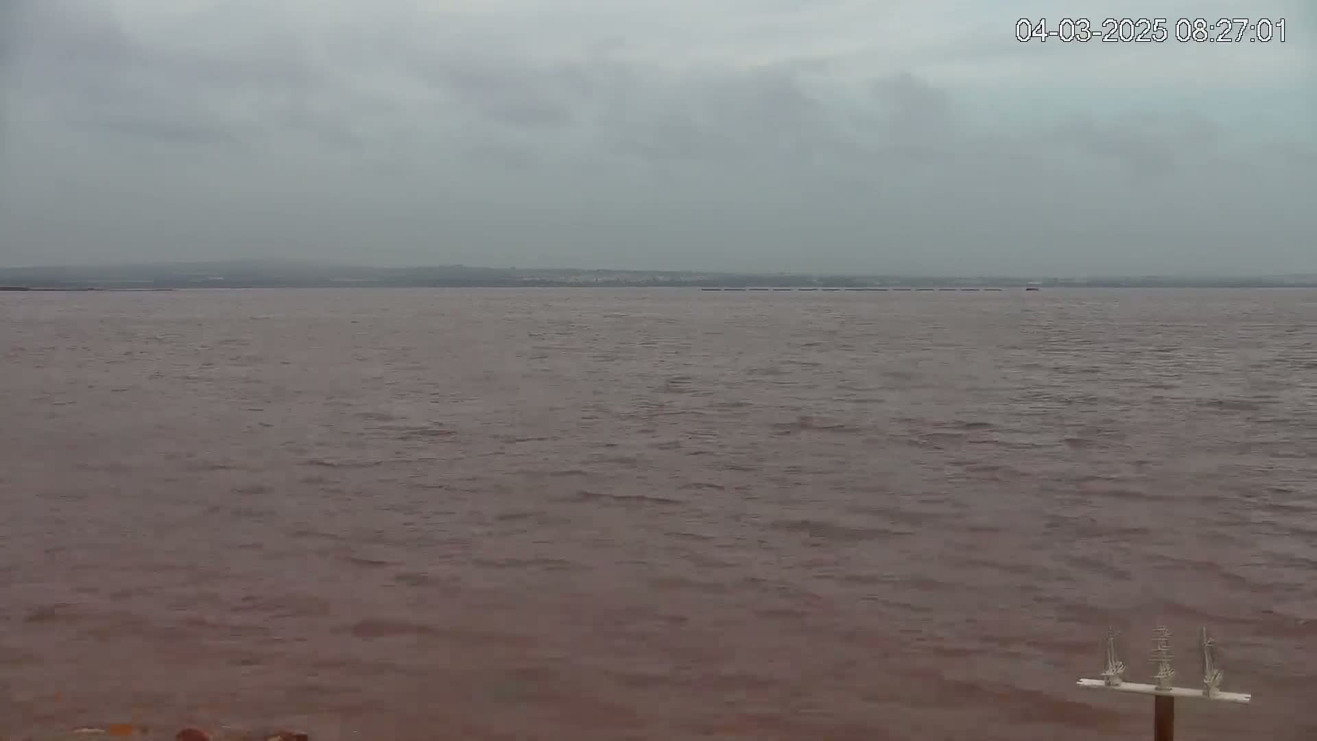 A wide shot of a calm, reddish-brown body of water under an overcast sky.