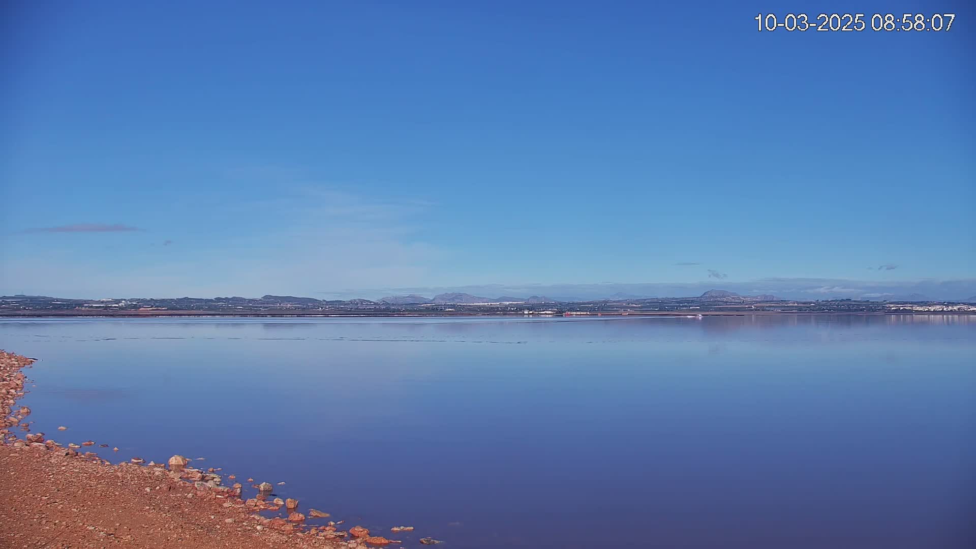 A calm, purplish-blue body of water stretches to a distant shoreline under a clear blue sky.