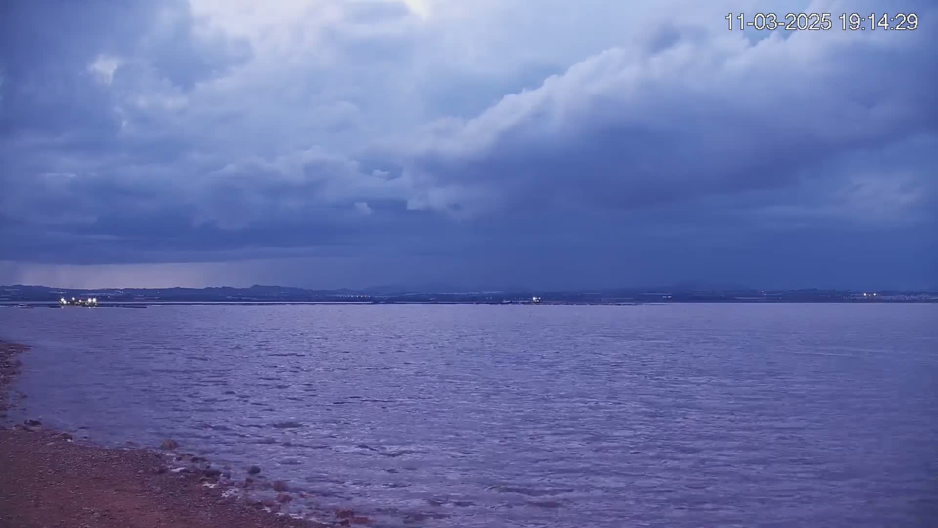 A calm body of water stretches to a distant shoreline under a cloudy, dusky sky.