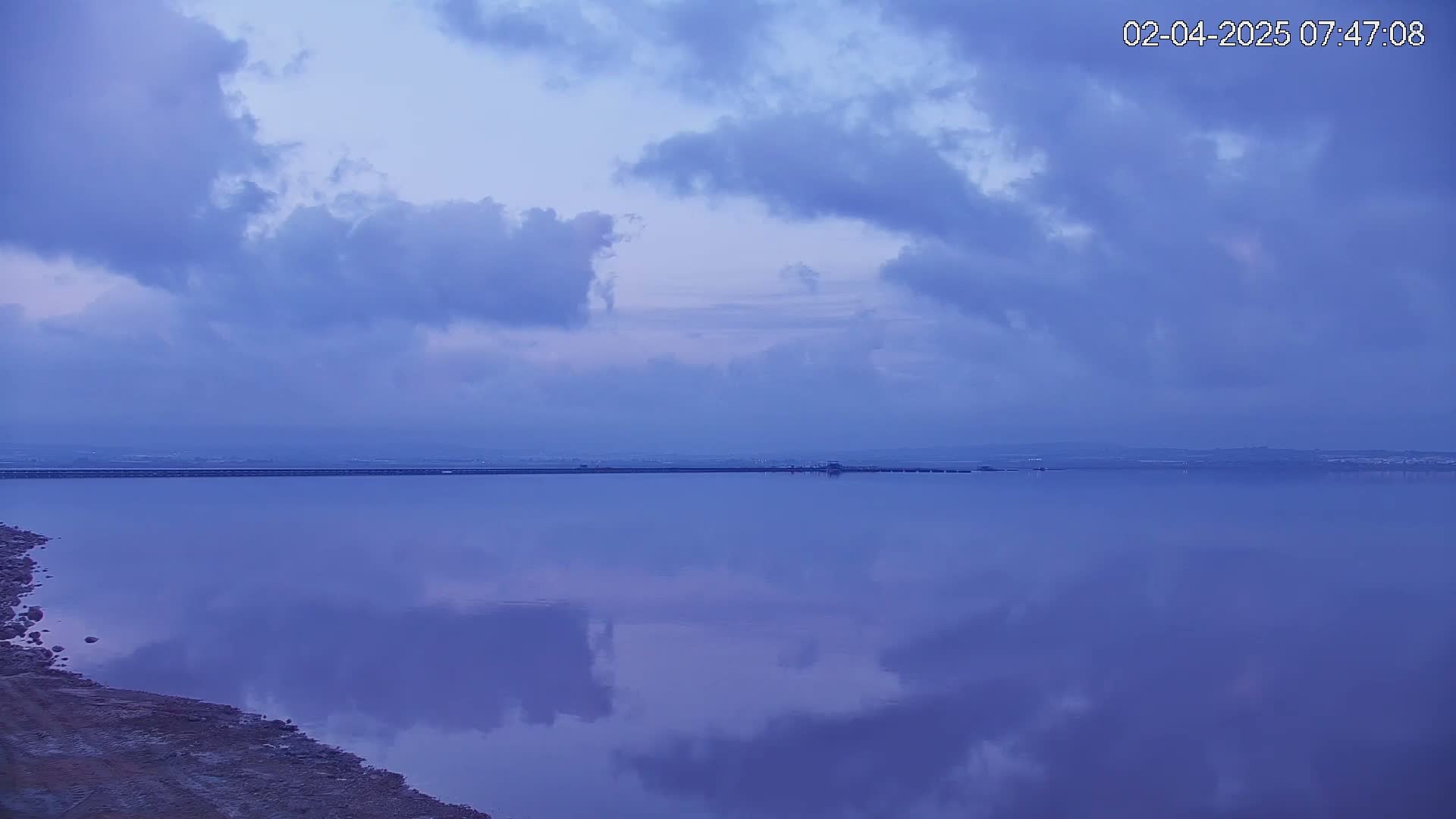 A calm body of water reflects a cloudy, twilight sky.
