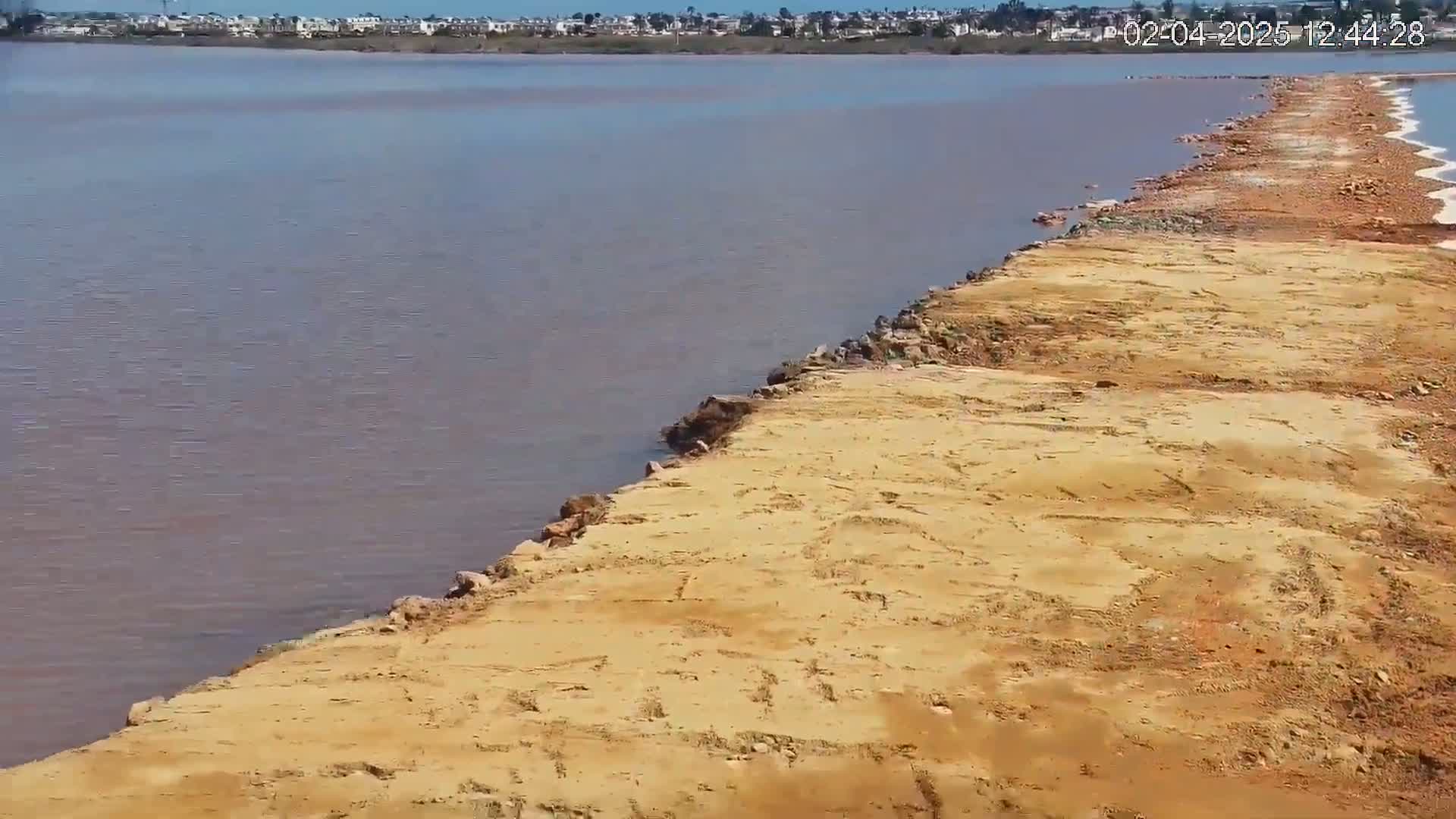 A long, sandy shoreline extends into a calm, pinkish-grey body of water under a clear sky.