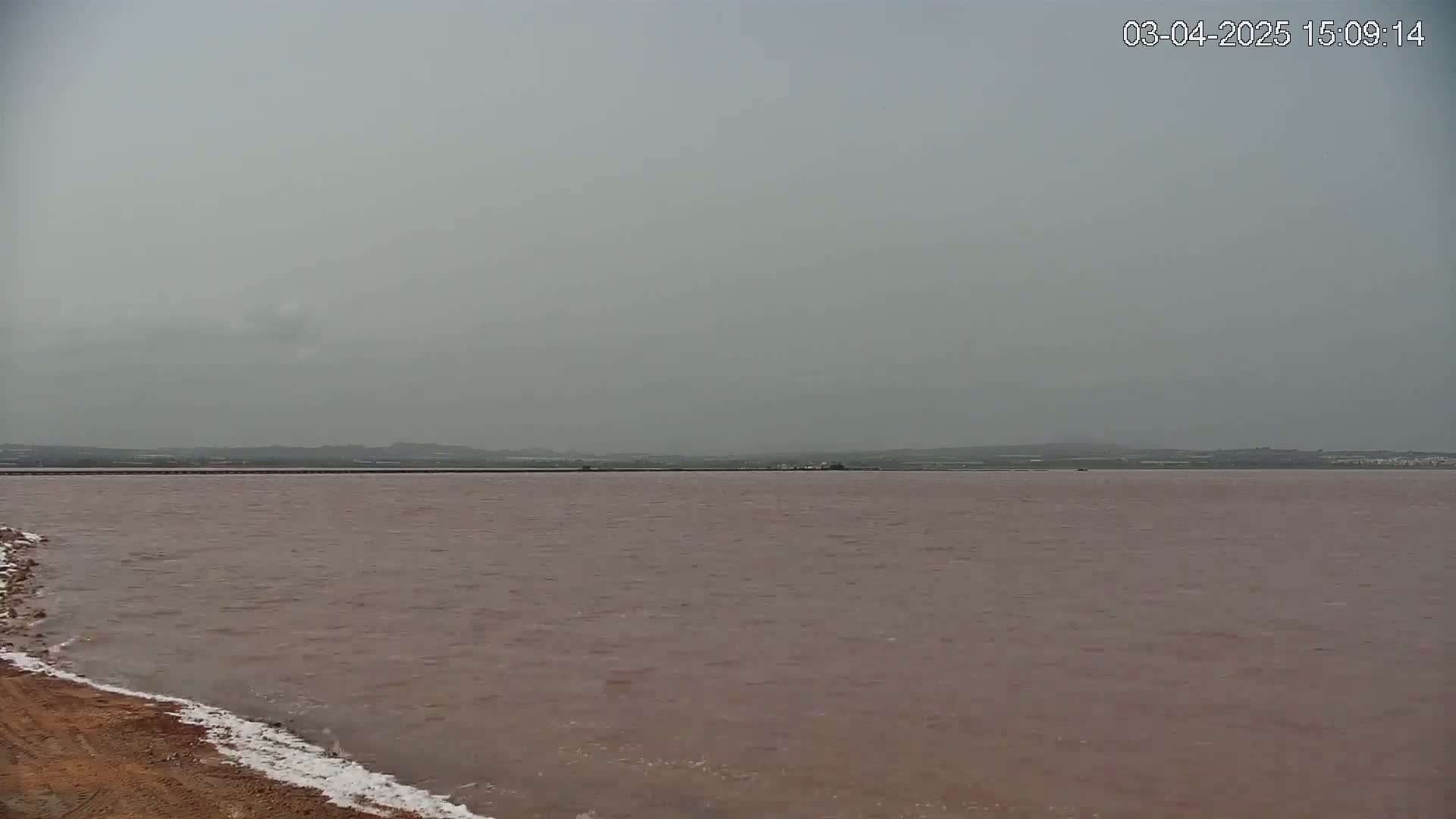 A pinkish-red body of water extends to a hazy, gray horizon under an overcast sky.