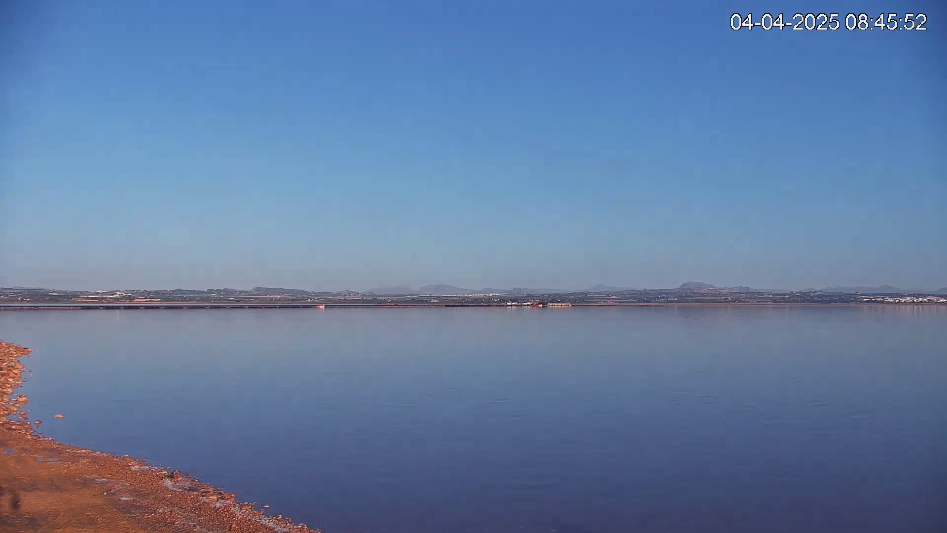 A calm body of water stretches to a distant shoreline under a clear blue sky.