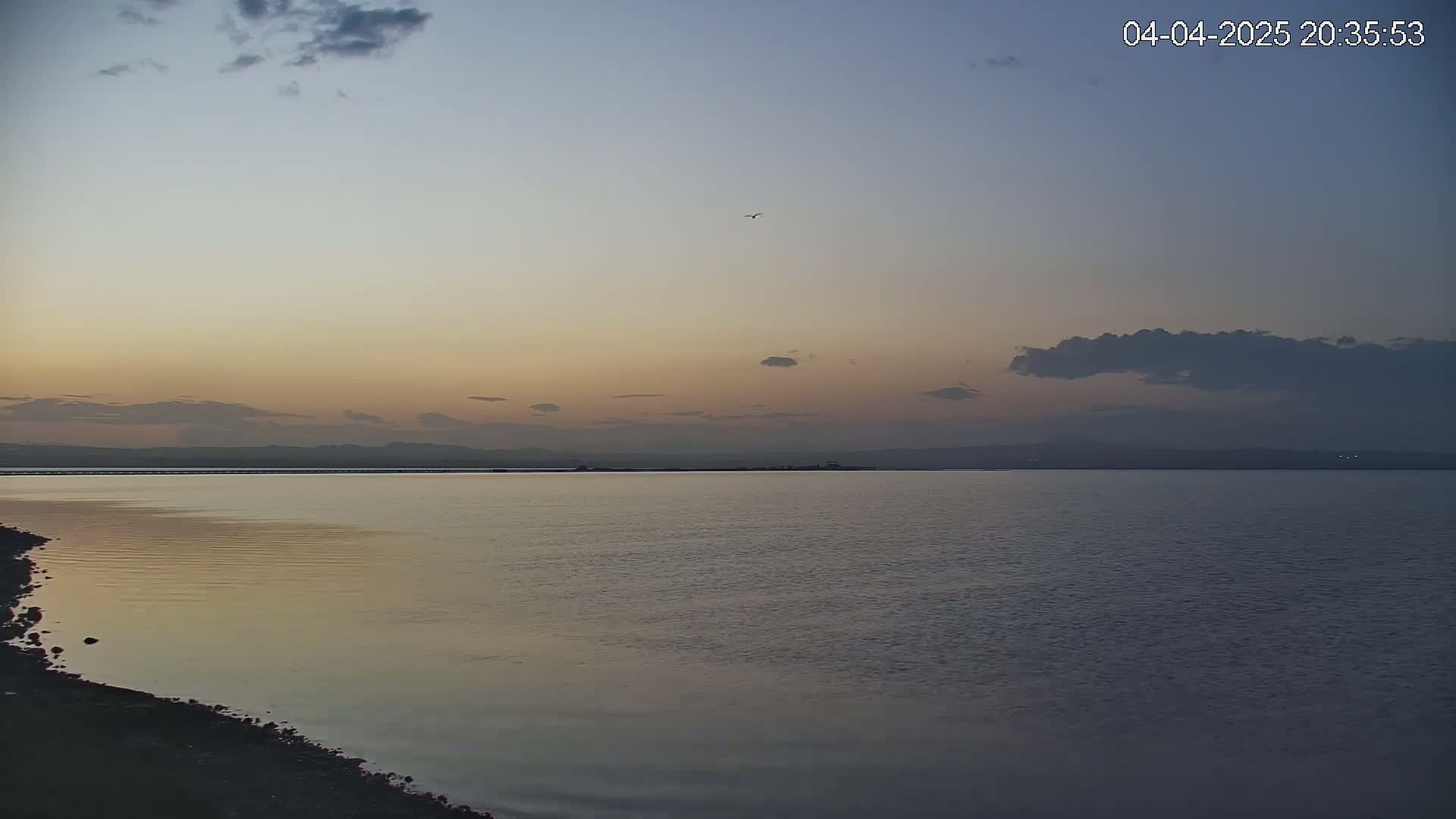 A calm body of water reflects a dusky sunset sky with a few clouds under a mostly clear twilight sky.