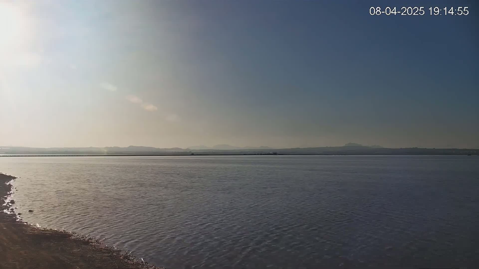 A calm body of water stretches to a hazy, distant shoreline under a clear, bright sky.