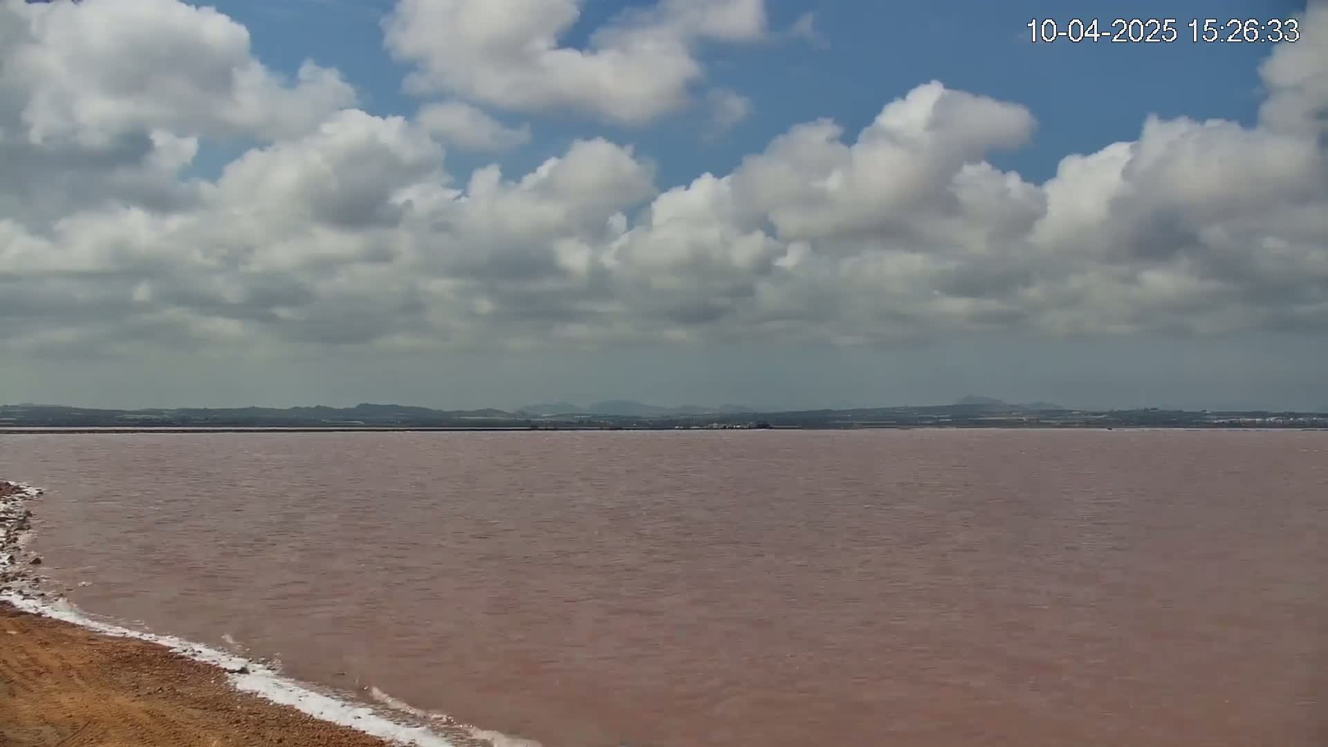 A pinkish-red body of water stretches to a distant shoreline under a partly cloudy sky.