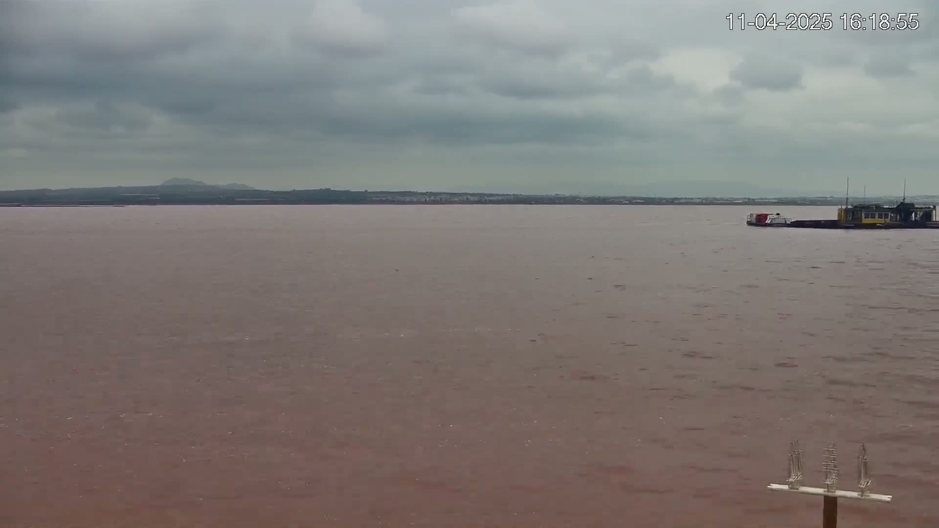 A barge is visible on a reddish-brown body of water under an overcast sky.