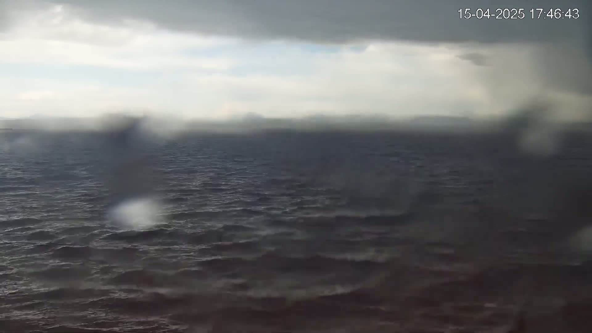 A dark, choppy sea is visible under a rainy, overcast sky.