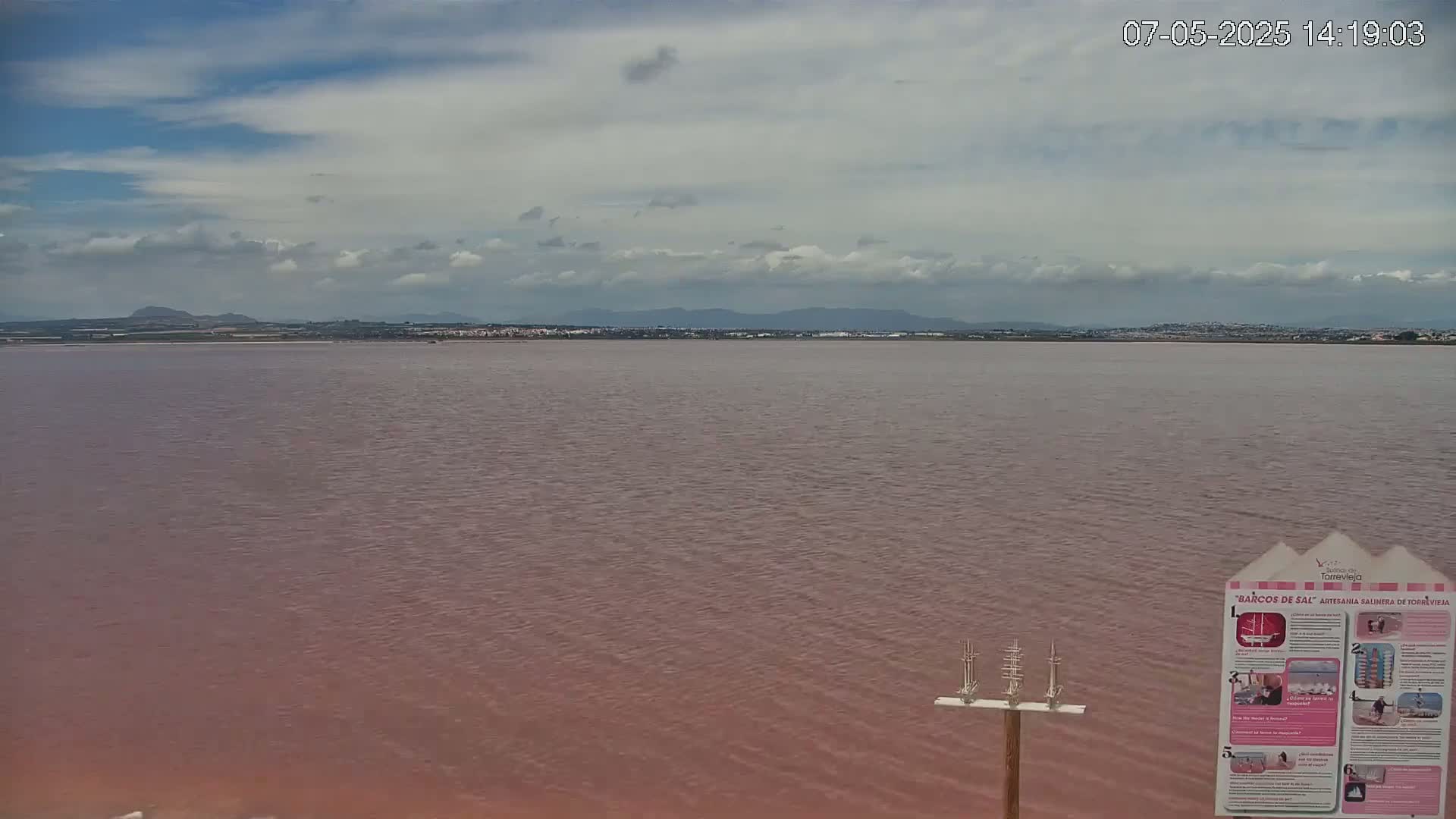 A pinkish-red body of water stretches to a distant shoreline under a partly cloudy sky.