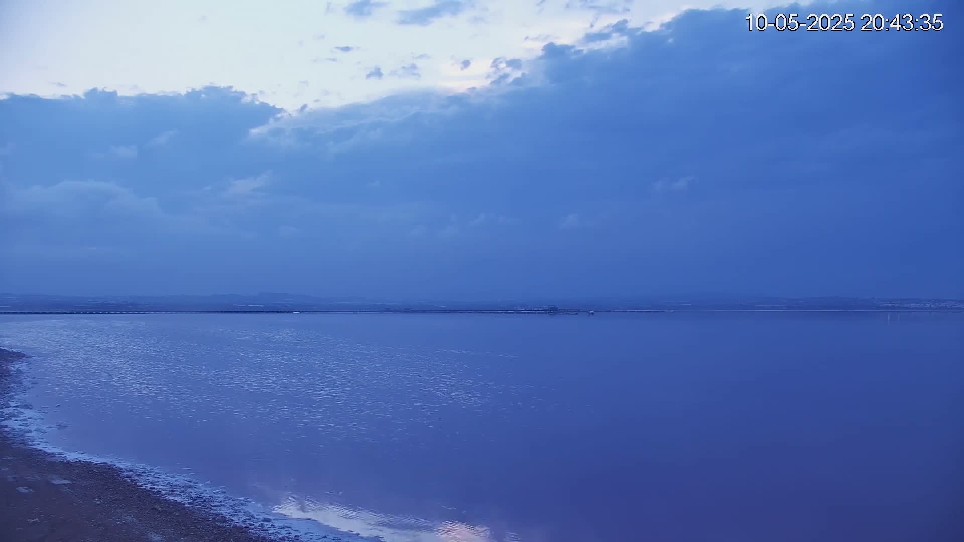 A calm, purplish-blue body of water stretches to a distant shoreline under a cloudy, twilight sky.