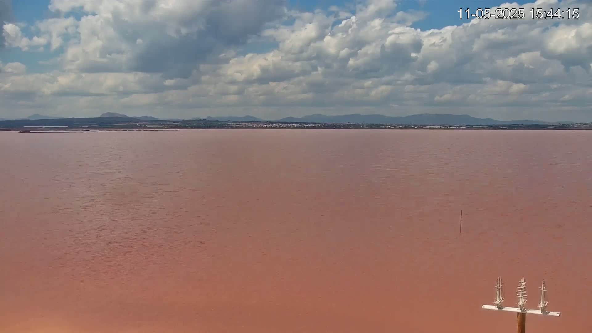 A pinkish-red body of water stretches to a distant shoreline under a partly cloudy sky.
