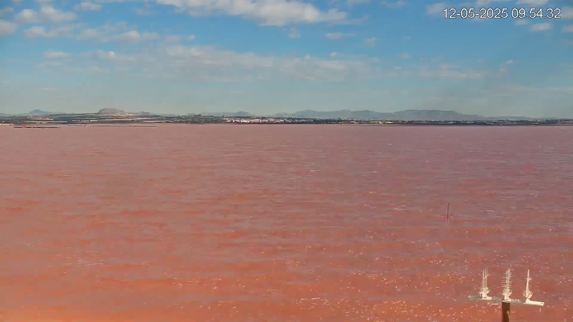 A pink body of water stretches to a distant shoreline under a mostly clear sky.