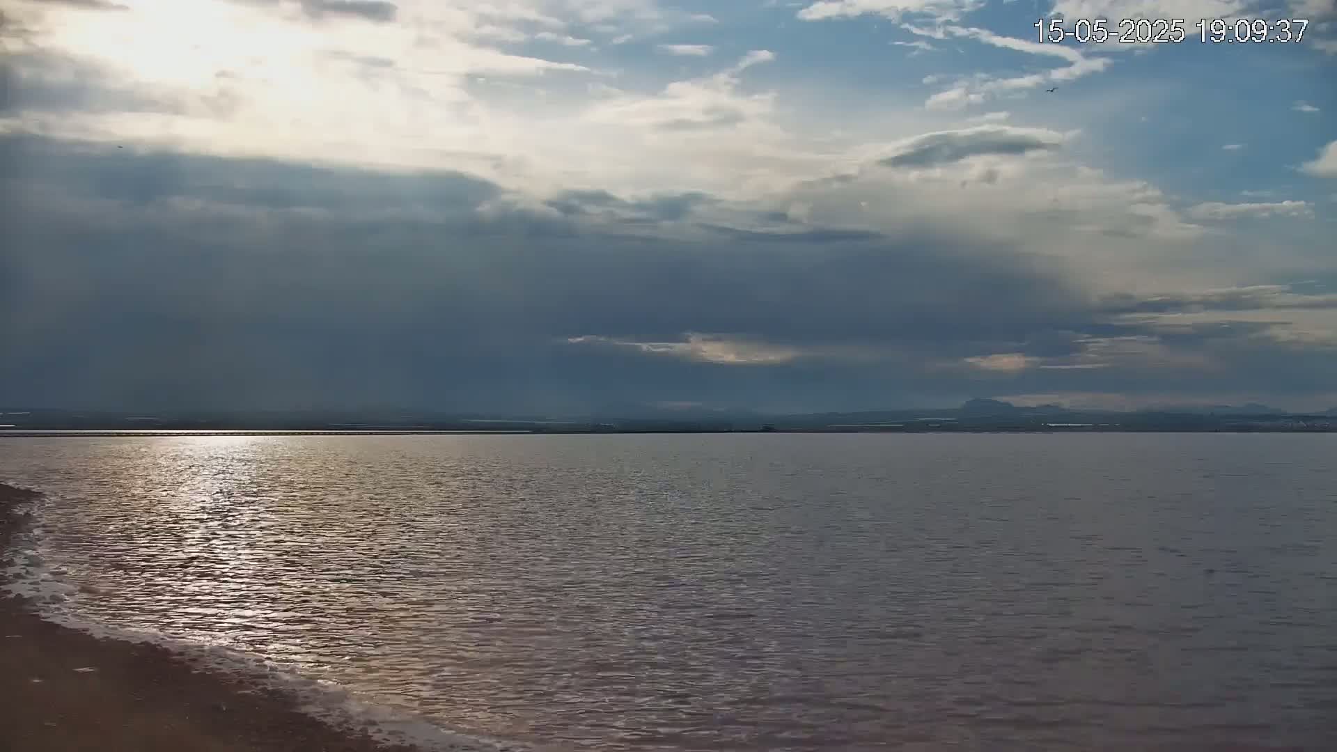 A calm body of water reflects the sun's rays under a partly cloudy sky.