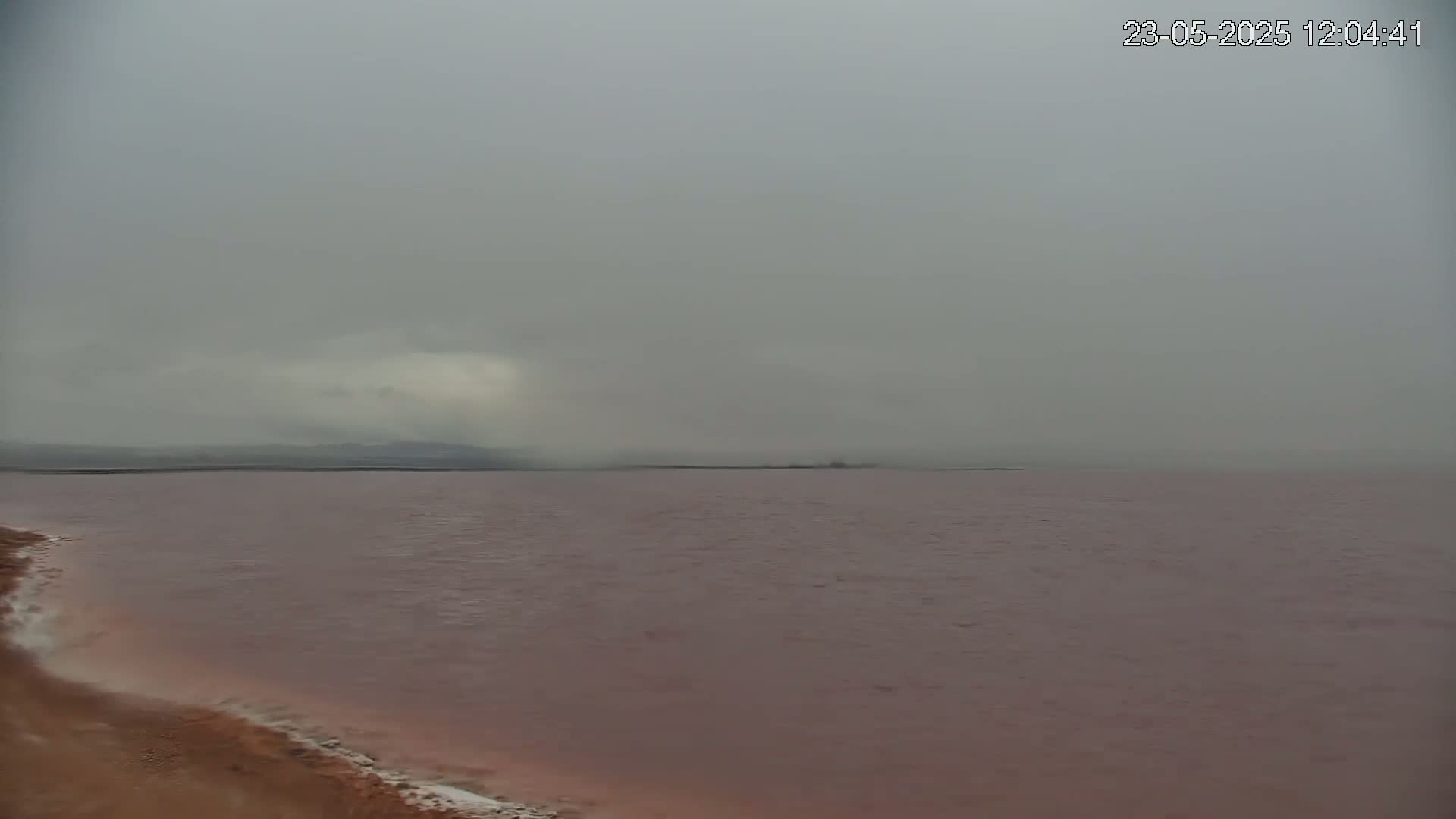A pinkish-red body of water stretches to a hazy, overcast horizon under a gray sky.
