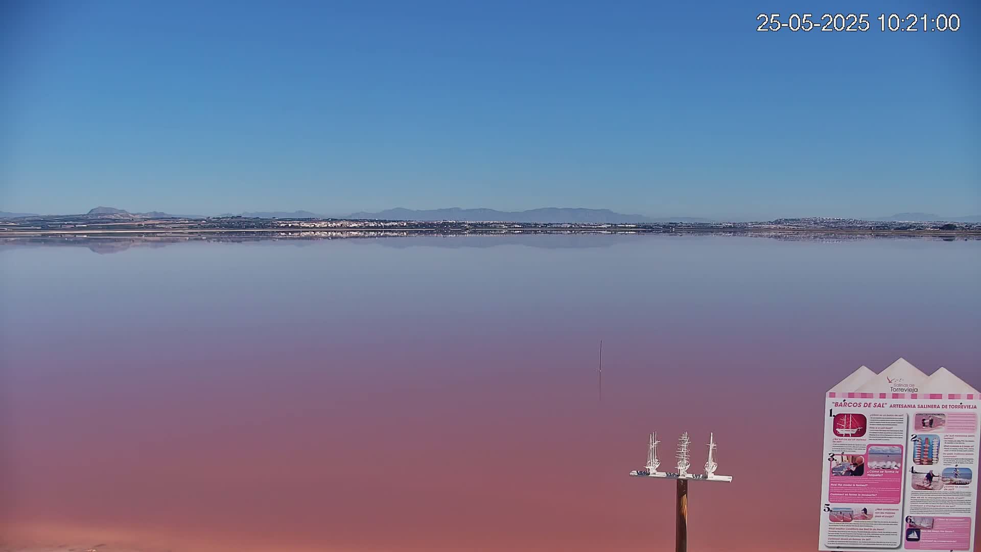 A calm, pink lake reflects a distant shoreline under a clear blue sky.